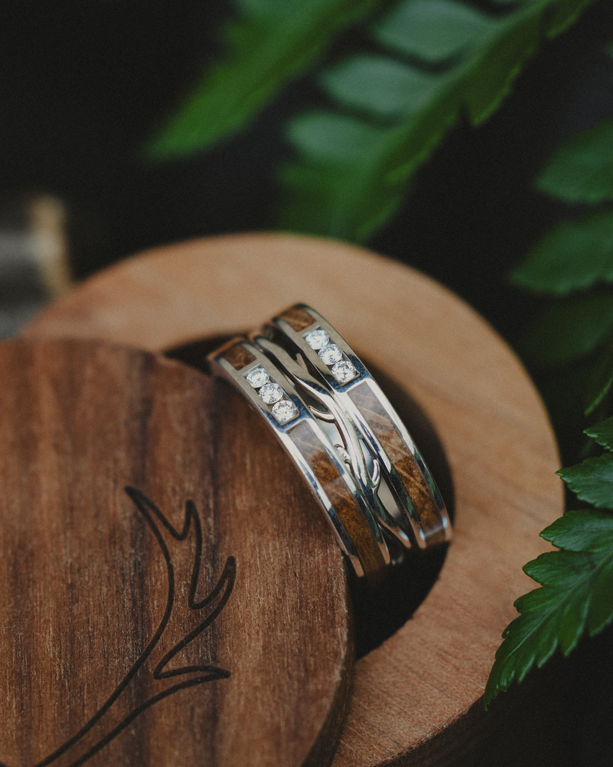 Silver wedding band with wood inlay and diamond accents in a wooden ring box against a natural background