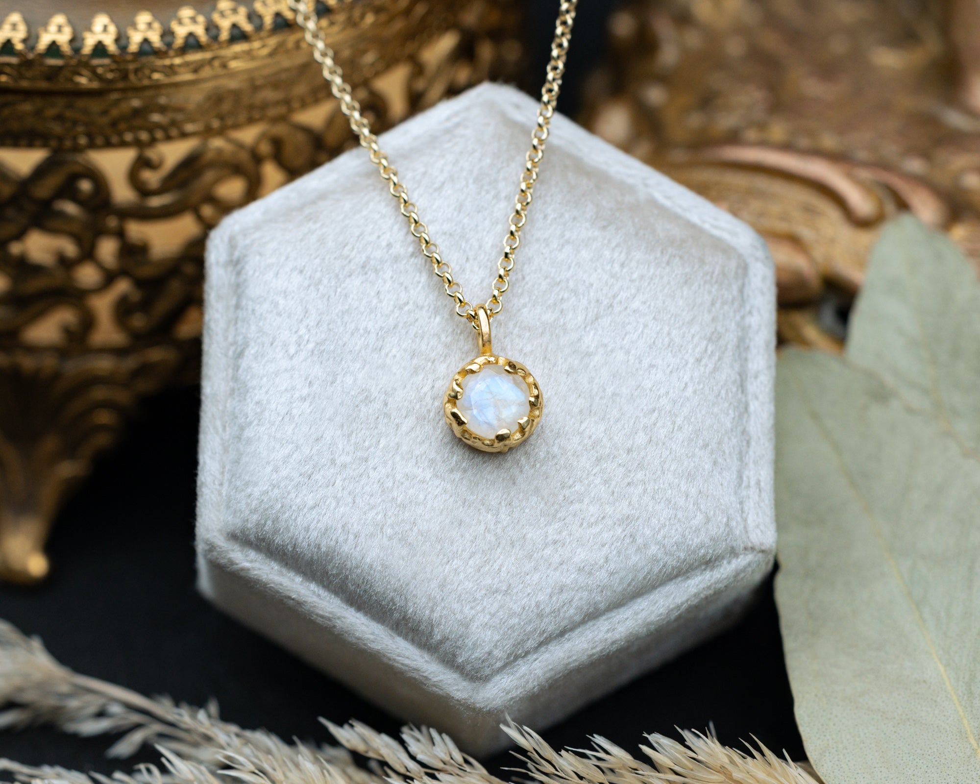 Gold necklace with a moonstone pendant on a white hexagonal stand with a decorative background