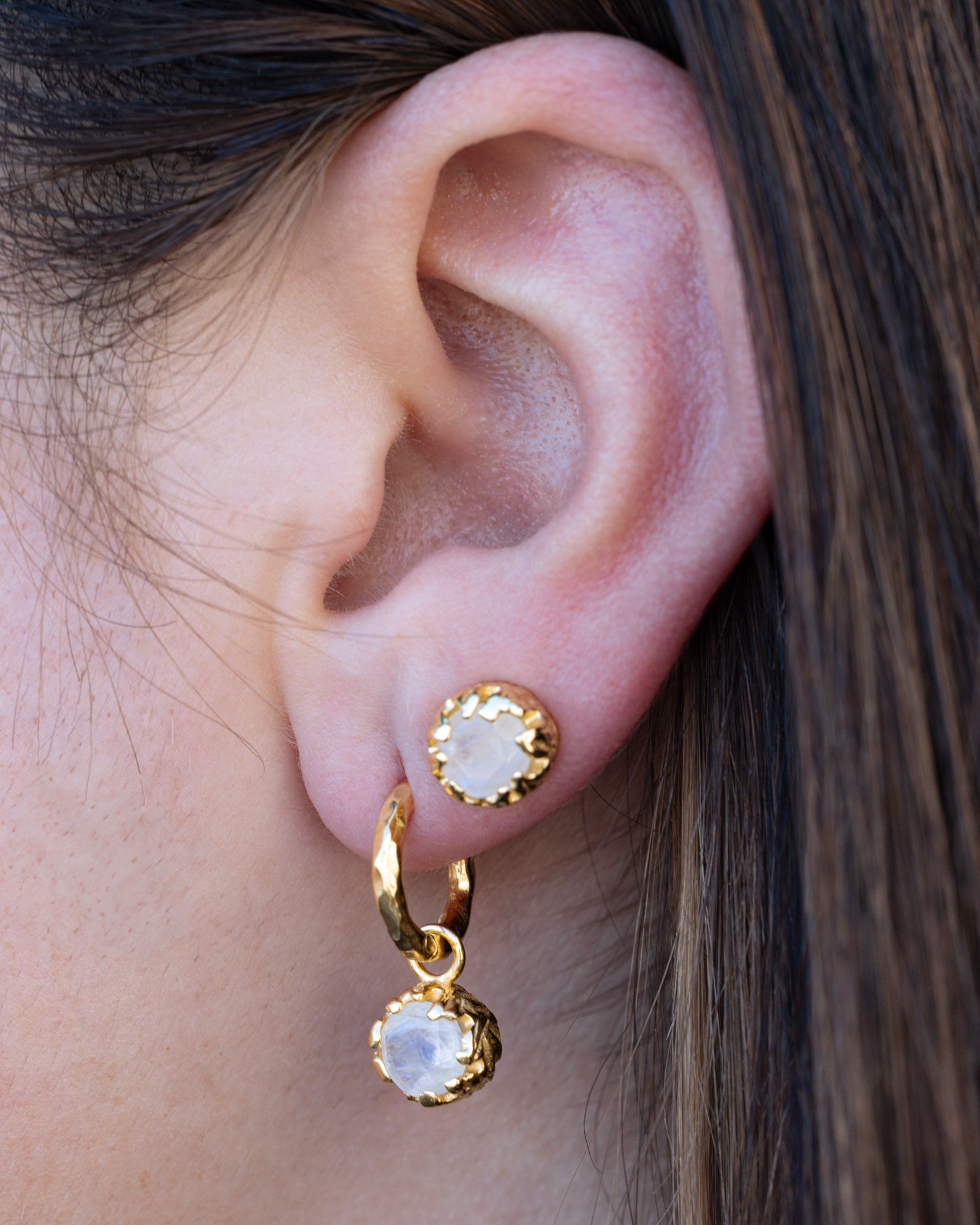 Close-up of an ear wearing gold hoop earrings with round, faceted moonstones.
