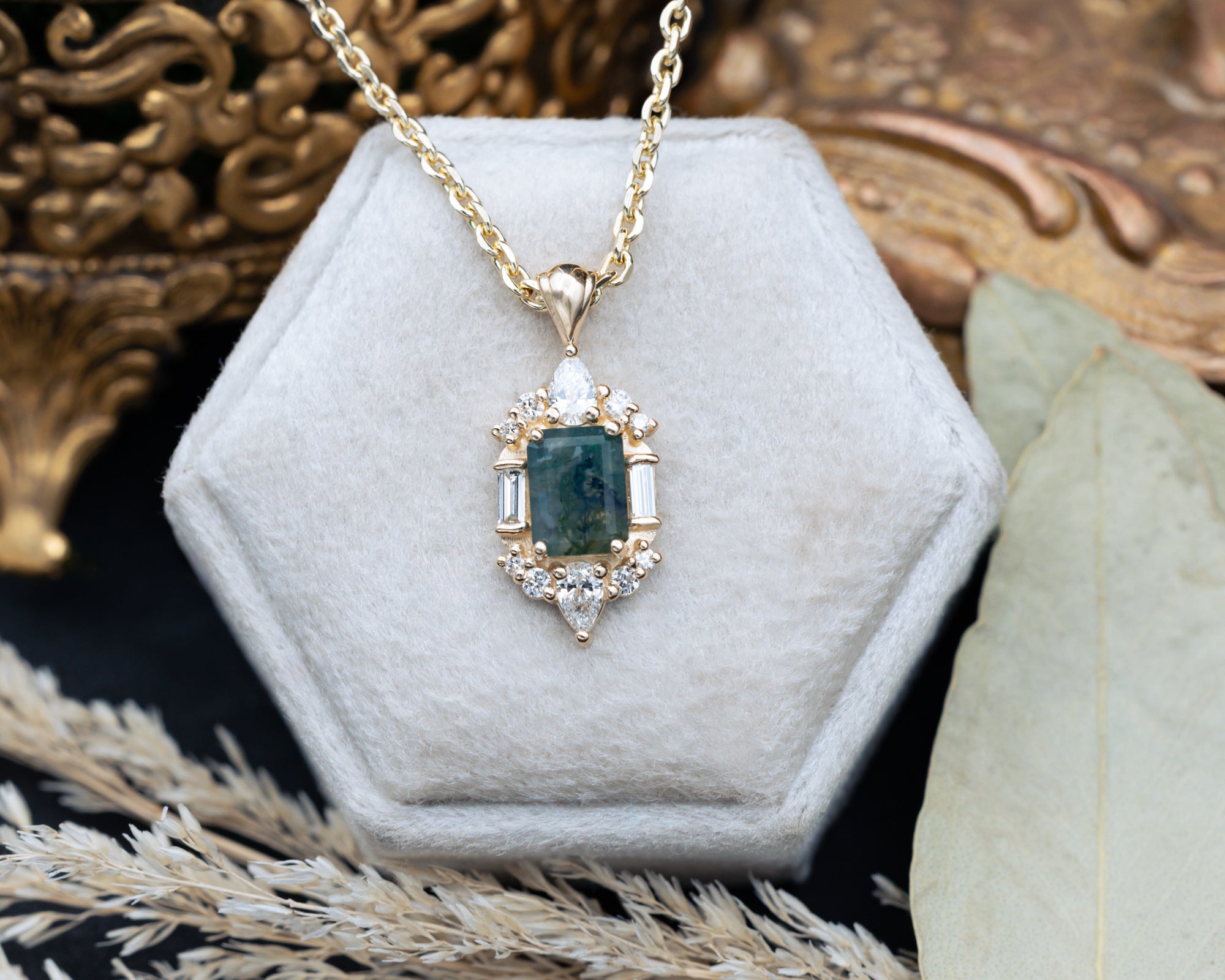 Gold necklace with a moss agate pendant on a hexagonal gray velvet stand.