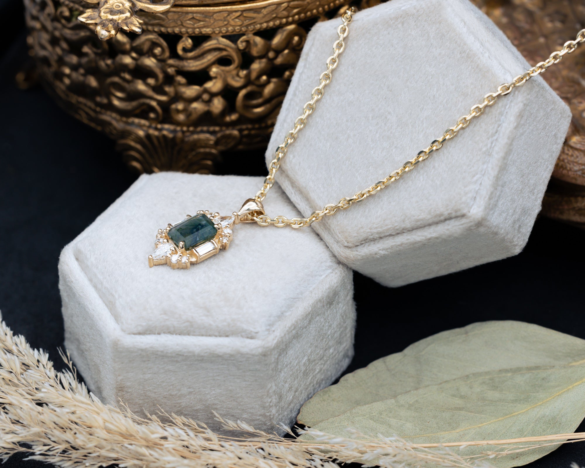 Gold necklace with a moss agate pendant on a hexagonal gray velvet stand.