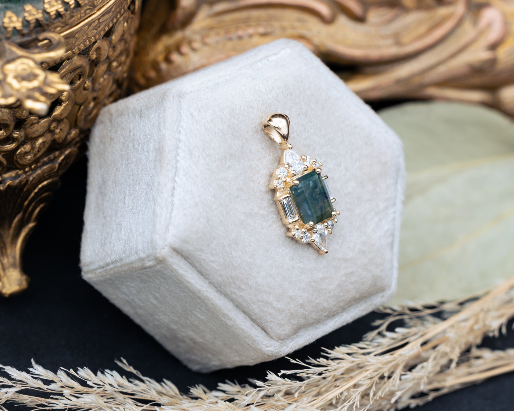 Gold moss agate pendant on a hexagonal gray velvet stand.