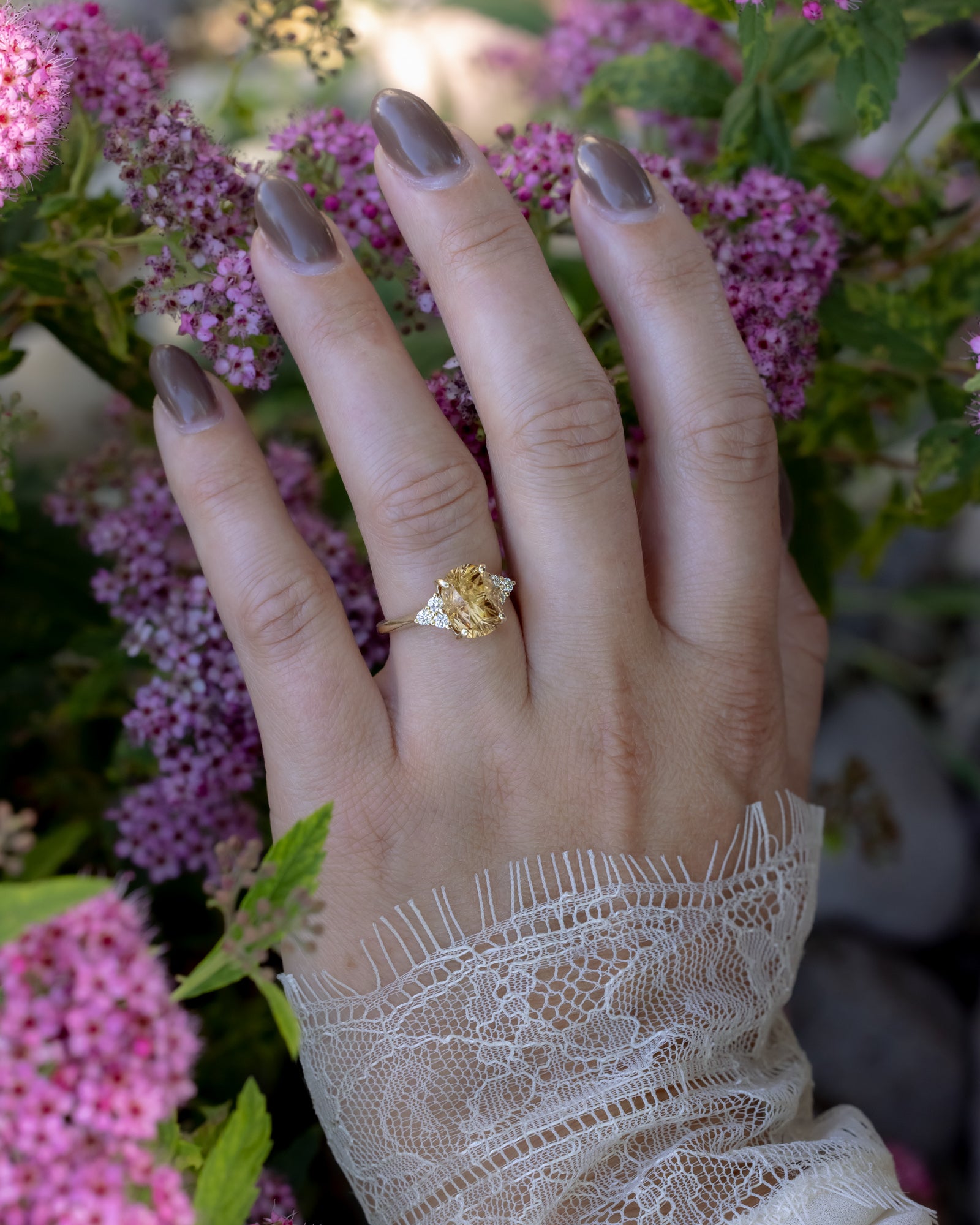 Hand wearing a gold ring with pink flowers in the background