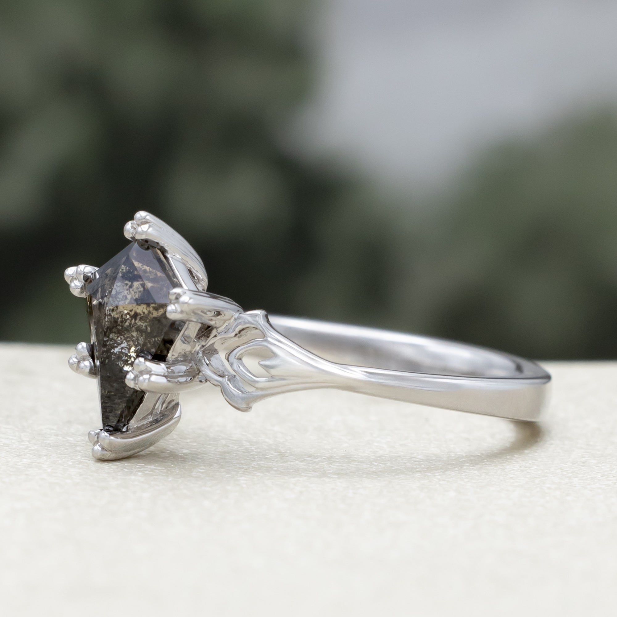 White gold ring with a kite cut salt & pepper diamond and intricate filigree against a blurred background