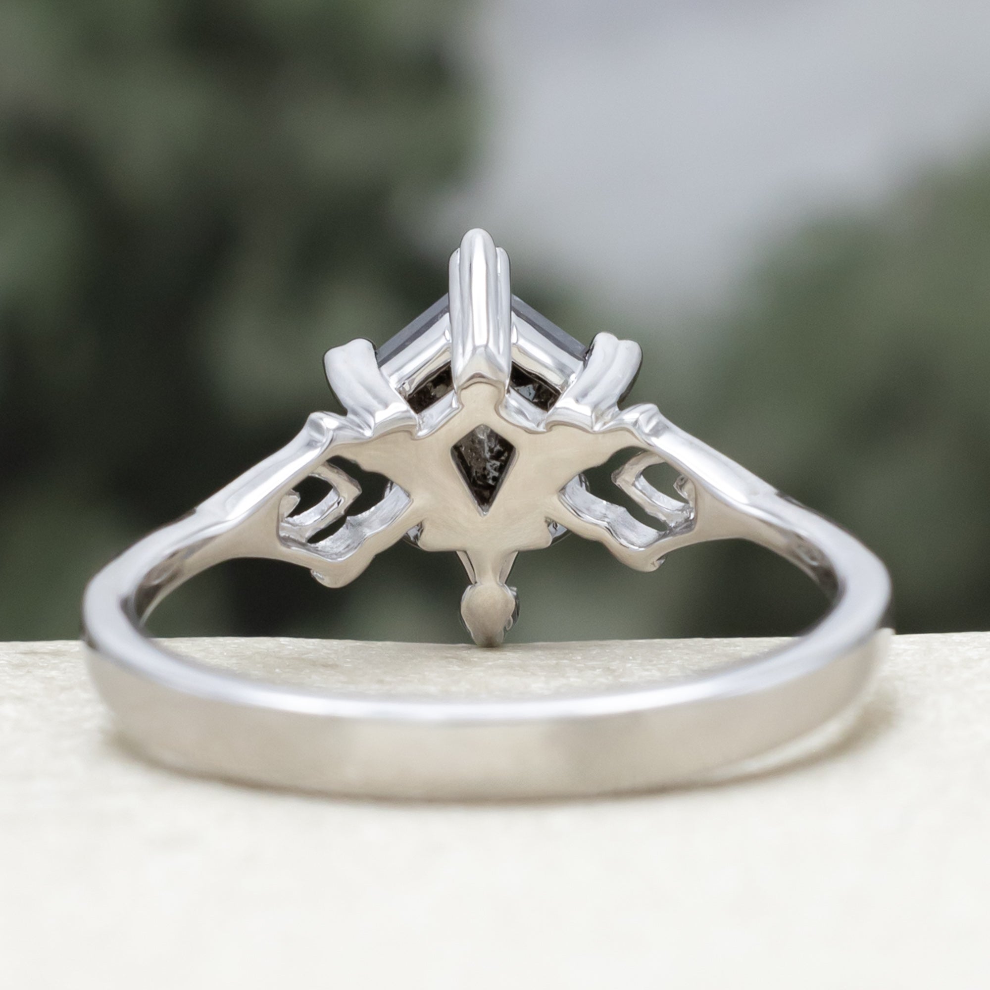White gold ring with a kite cut salt & pepper diamond and intricate filigree against a blurred background