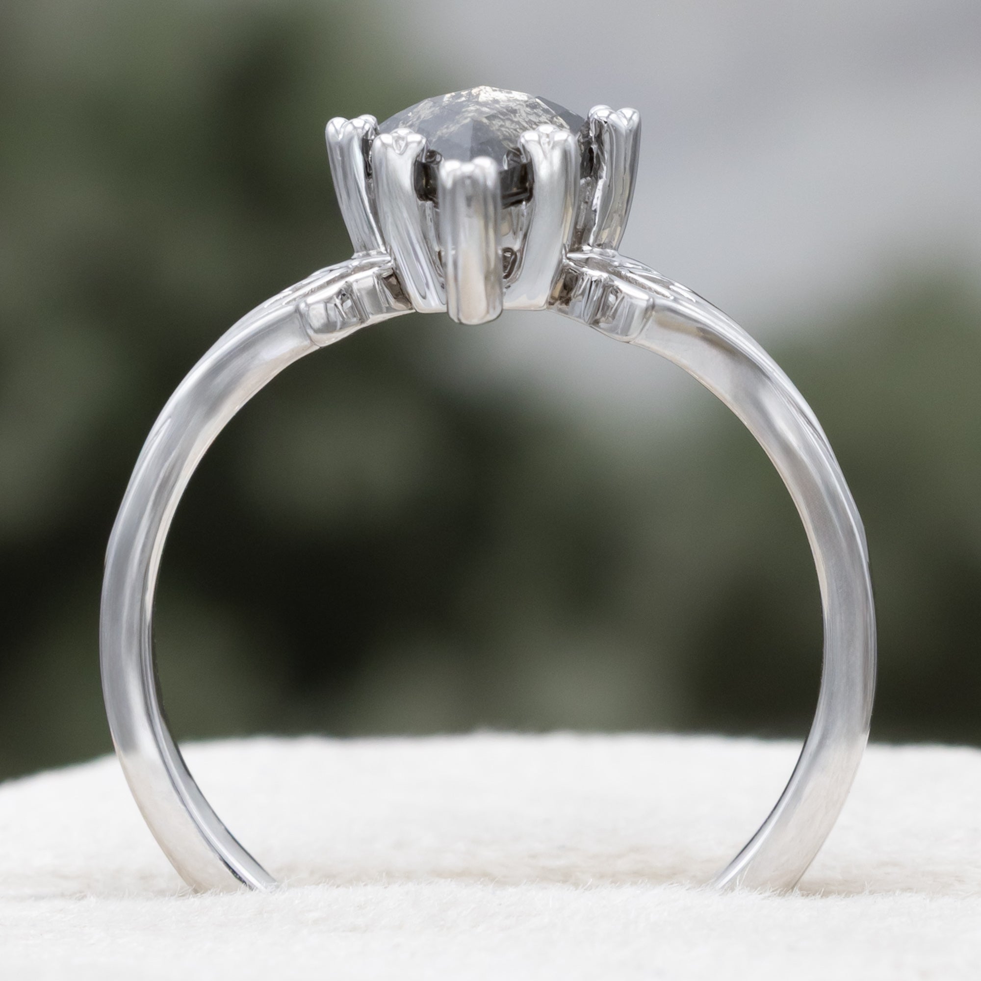 White gold ring with a kite cut salt & pepper diamond and intricate filigree against a blurred background