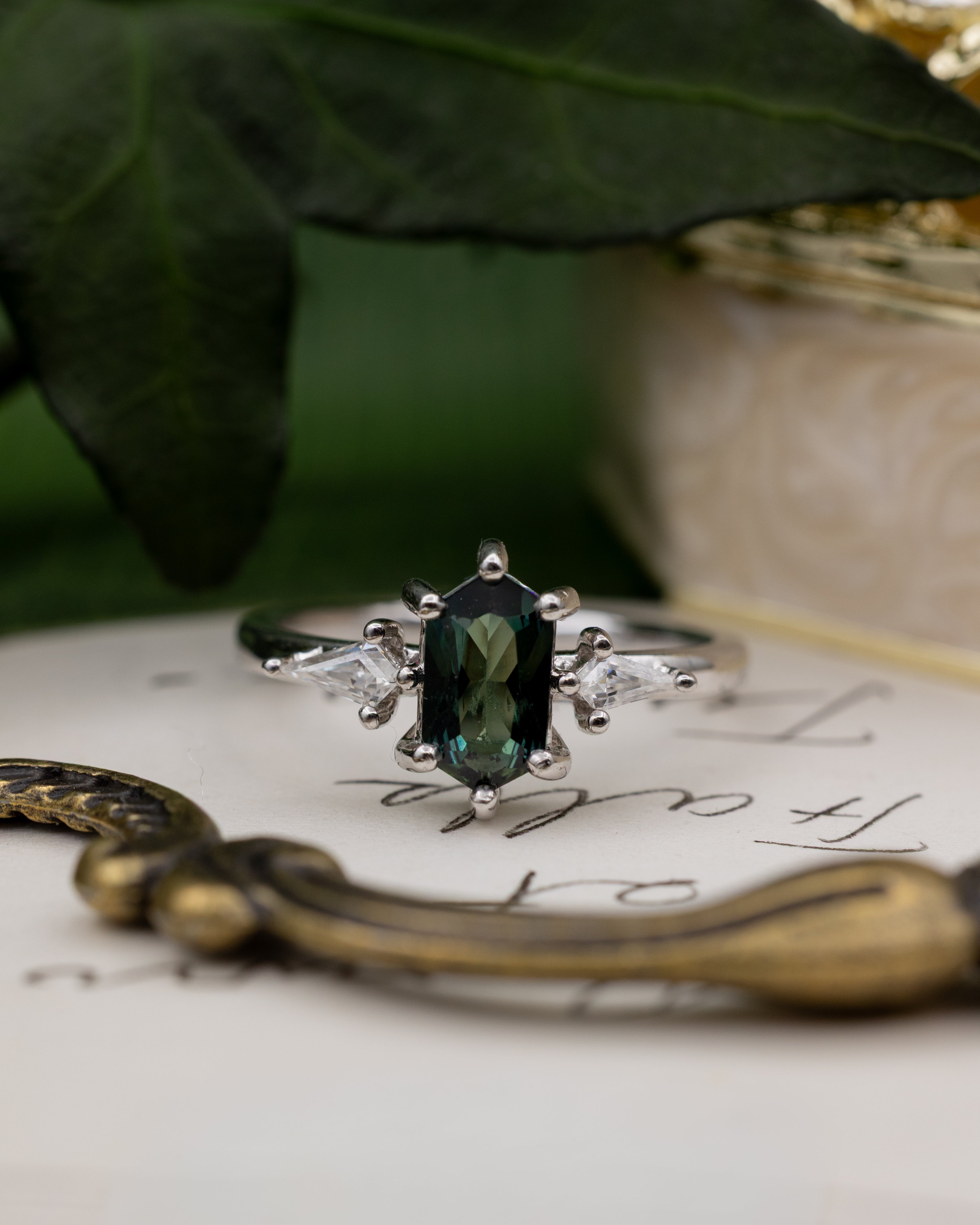 White gold ring with a green sapphire on an old letter with decorative elements.