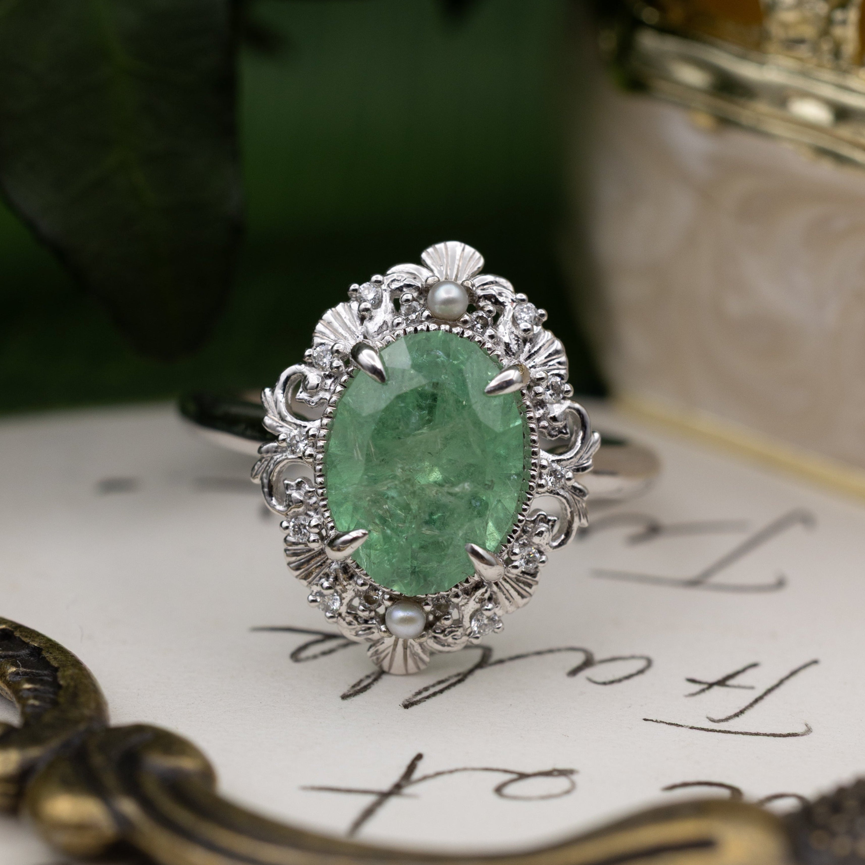 White gold ring with a green tsavoirte garnet on a decorative surface with leaves in the background