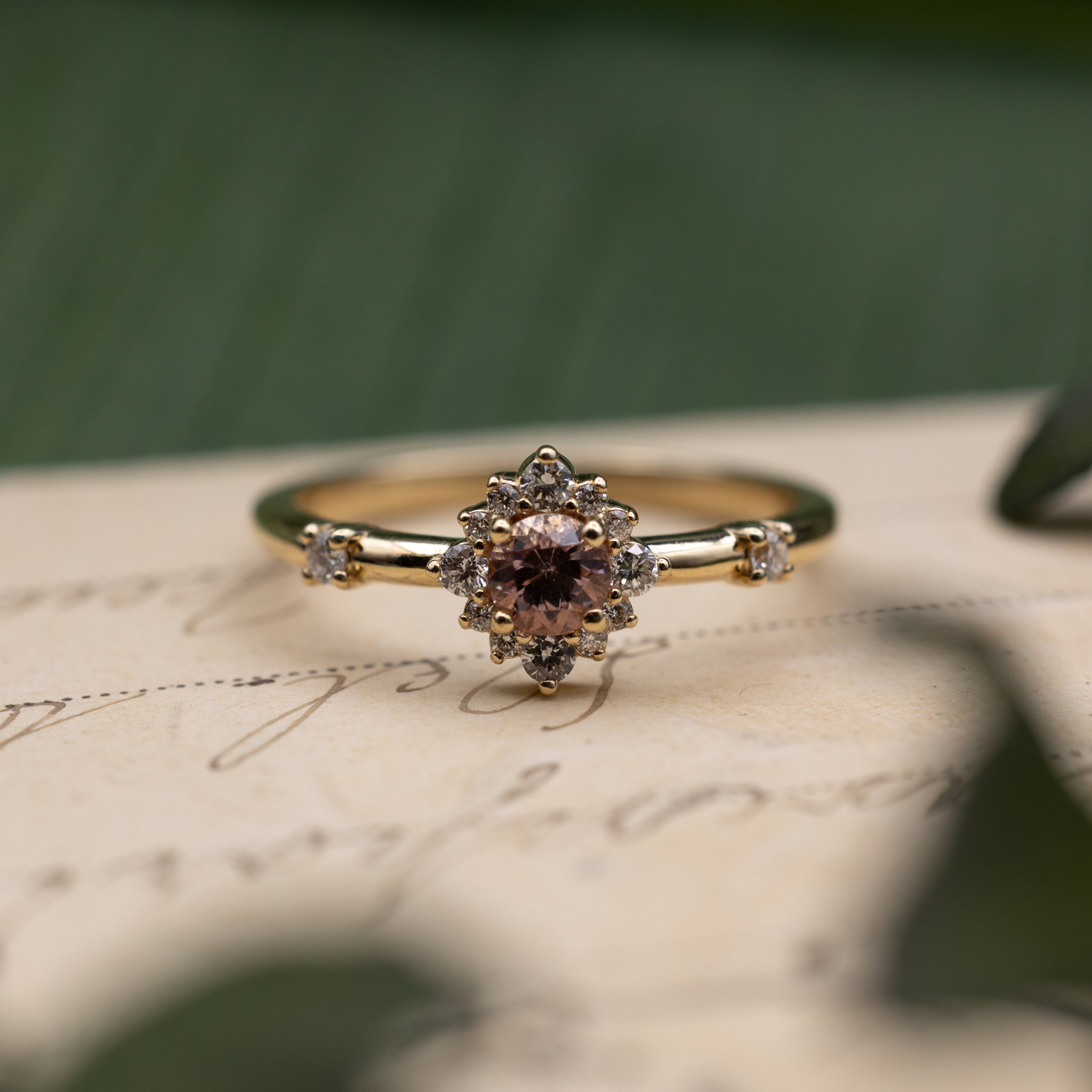 Yellow gold ring with dragon garnet center stone and diamond accents on a vintage letter against a blurred green background