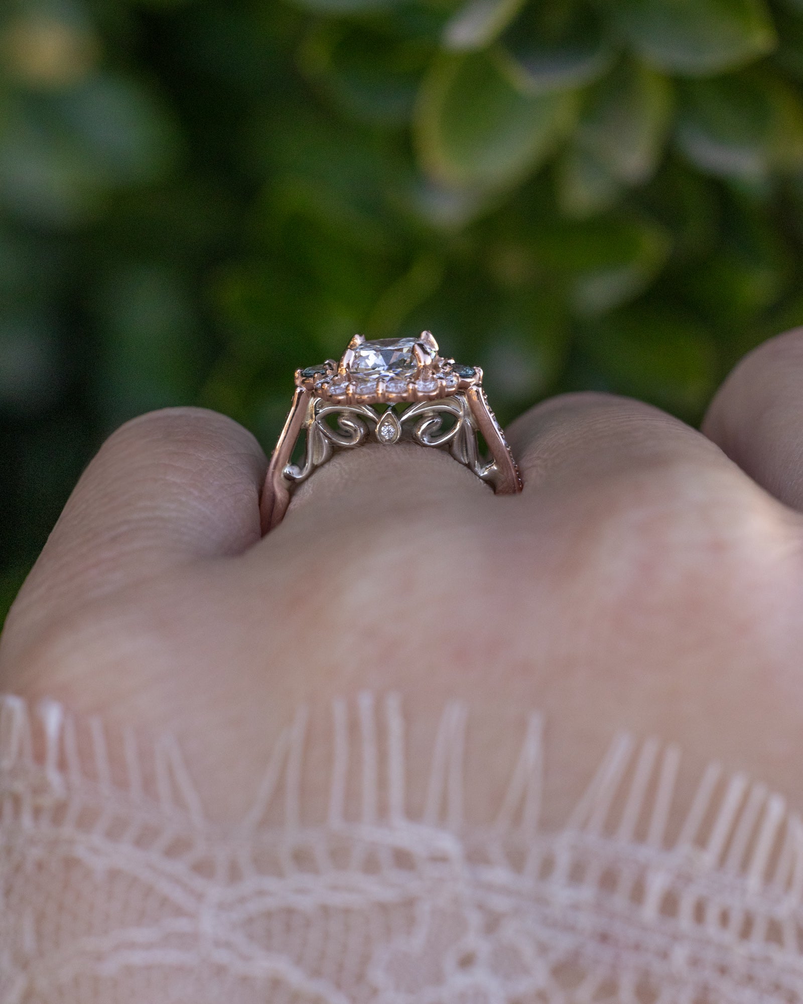 Rose gold ring with a diamond on a finger against a blurred green background
