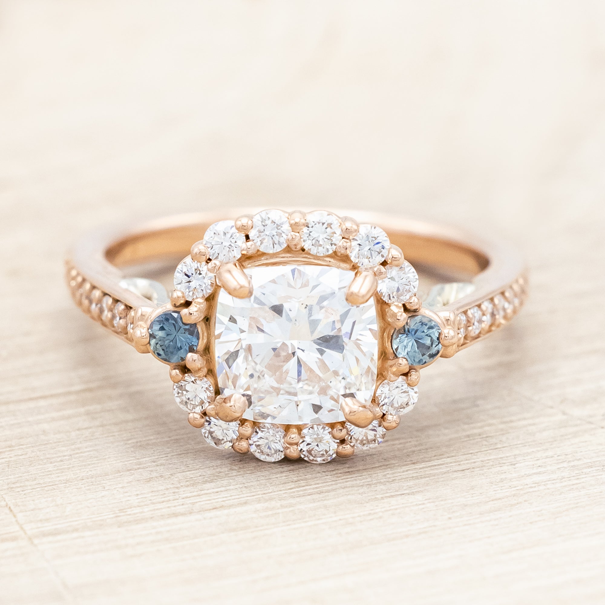 Rose gold ring featuring a large lab diamond with diamond and sapphire accents on a neutral background