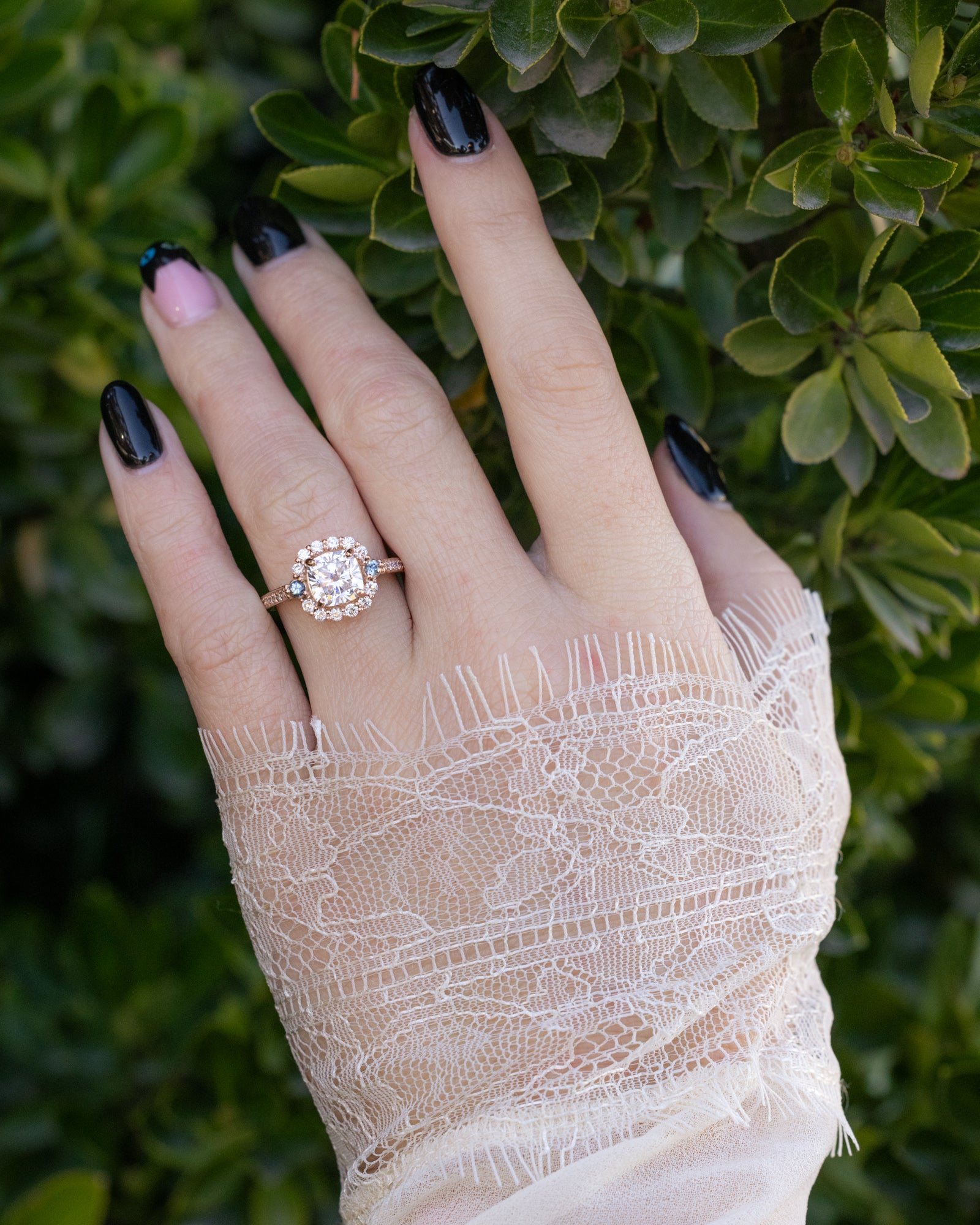 Hand wearing a diamond ring with a lace glove against a green leafy background