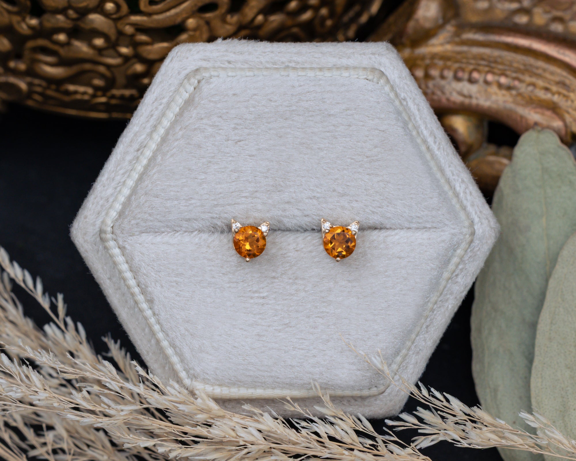 Pair of citrine cat-shaped stud earrings on a white cushion against a decorative background