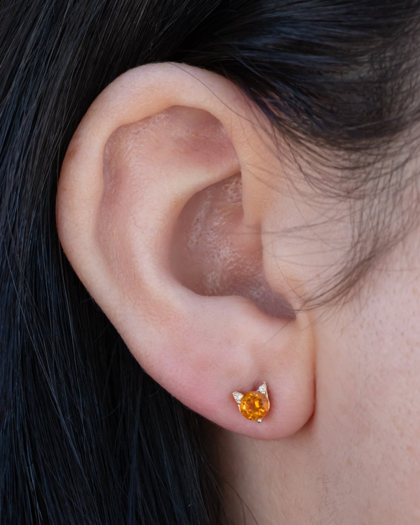 Citrine cat earring on the ear against dark hair