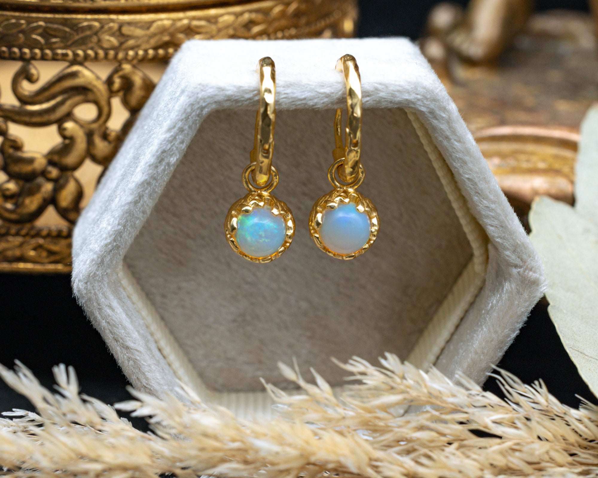 Gold earrings with opal stones in a hexagonal jewelry box on a decorative surface.