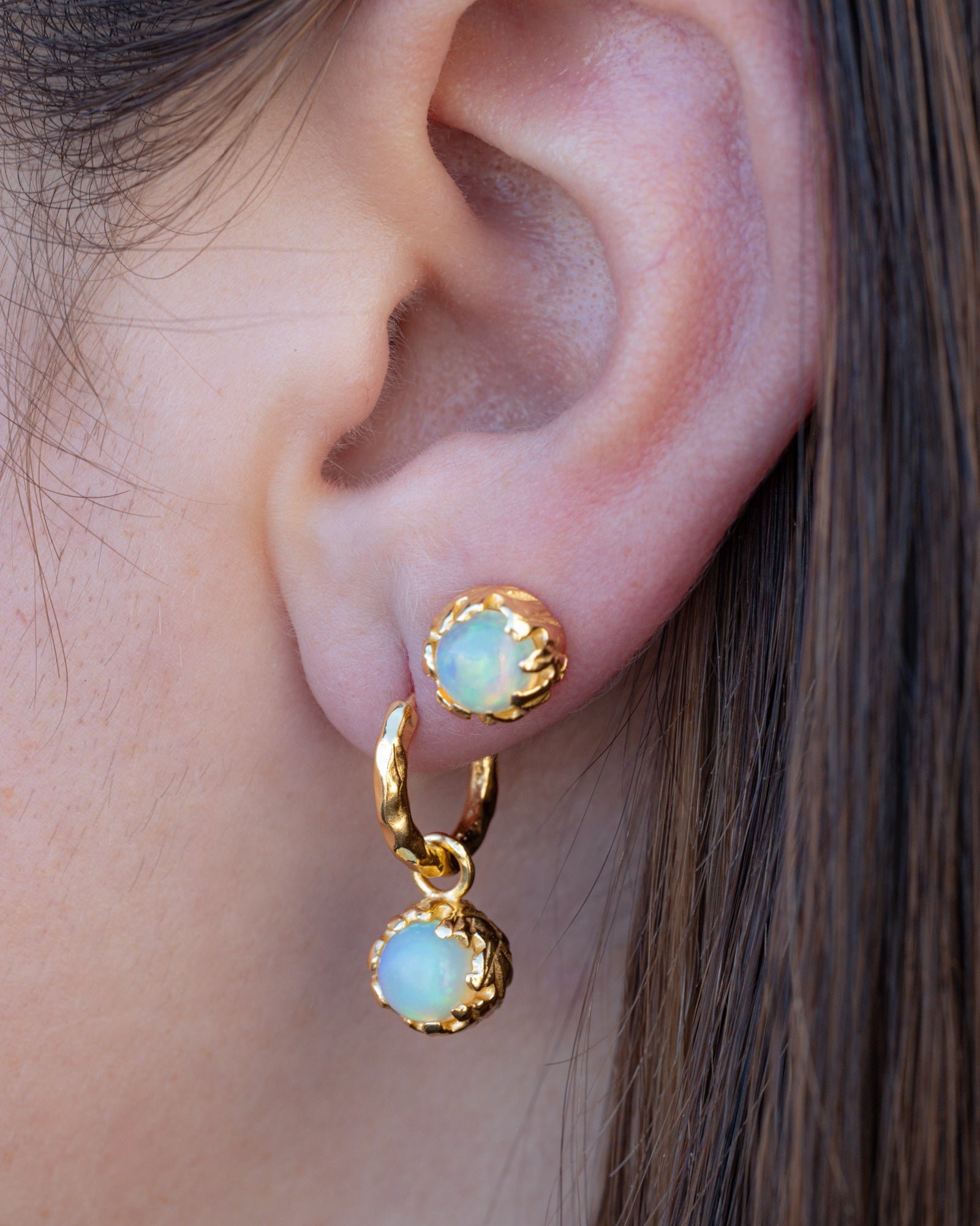 Close-up of an ear wearing gold earrings with opal stones.