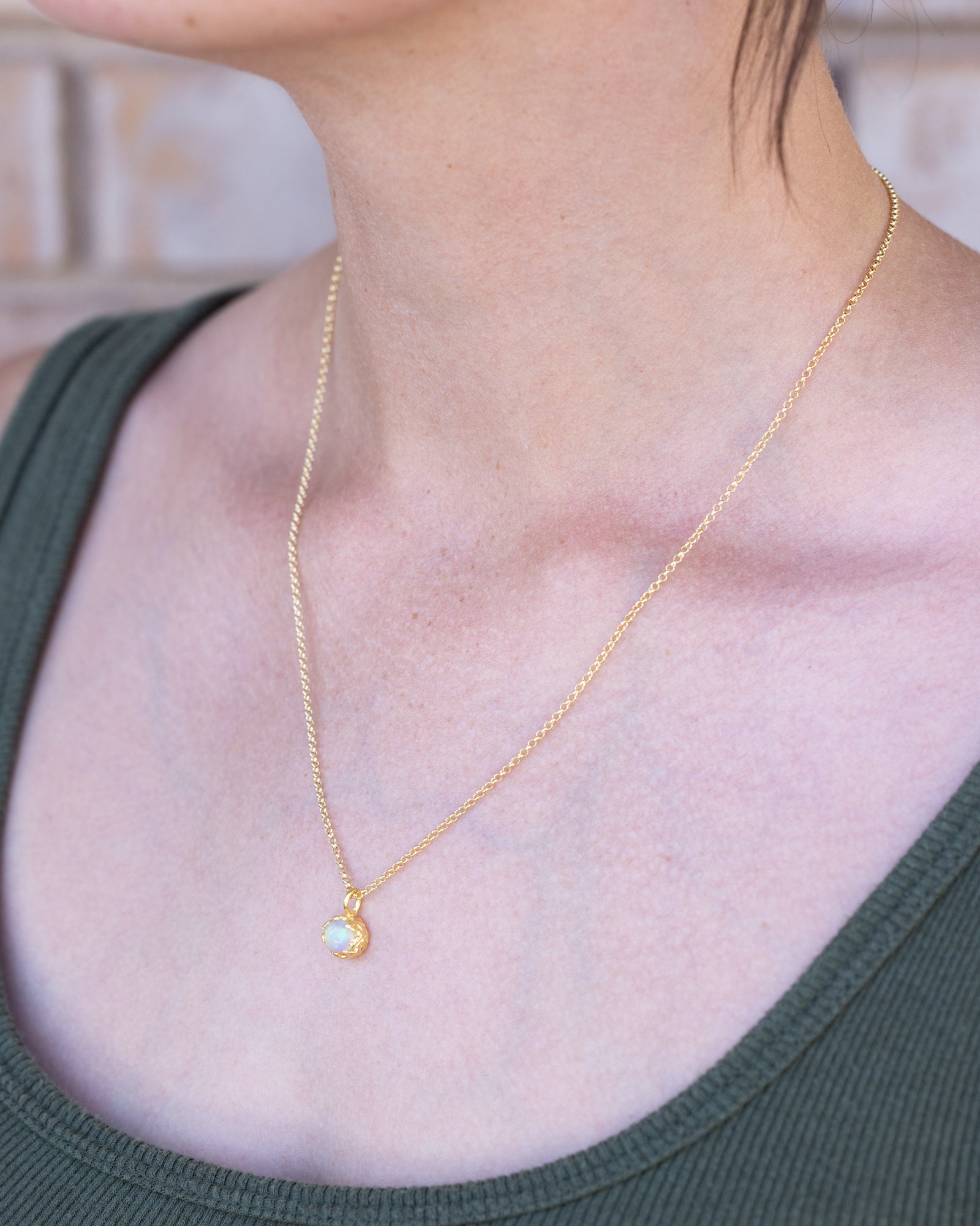 Gold necklace with a pendant worn by a person in a green top.