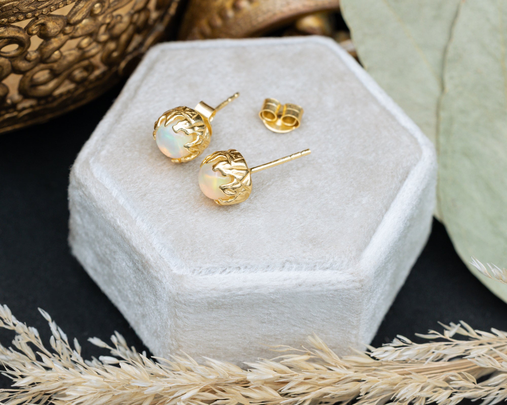 Gold earrings with opal stones on a white hexagonal jewelry box.