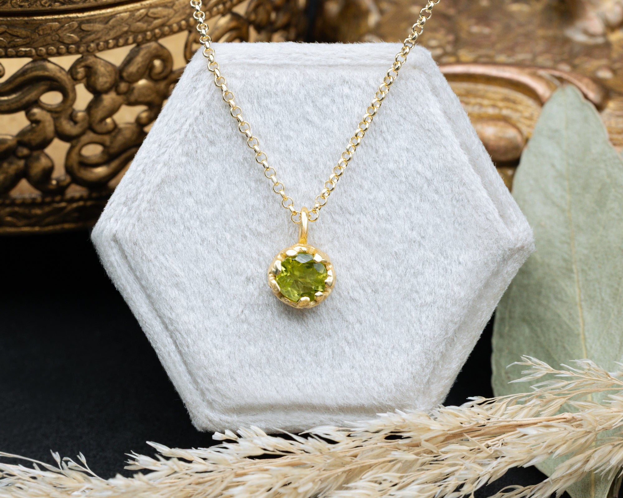 Gold necklace with a green peridot pendant on a white hexagonal stand.