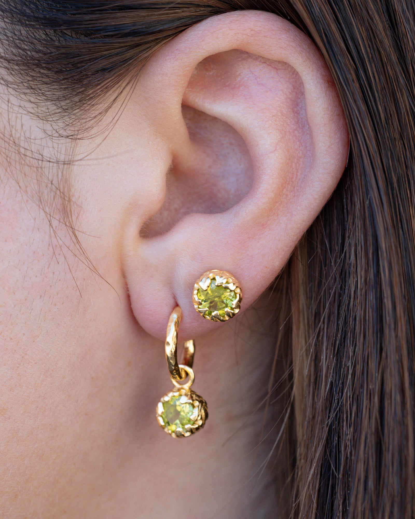 Close-up of an ear wearing gold hoop earrings with green peridot