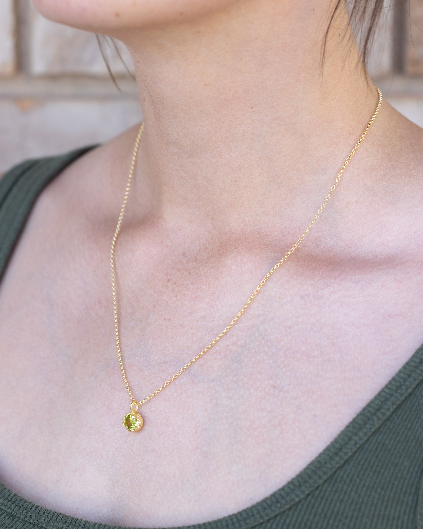 Gold necklace with a green peridot worn by a person in a green top.