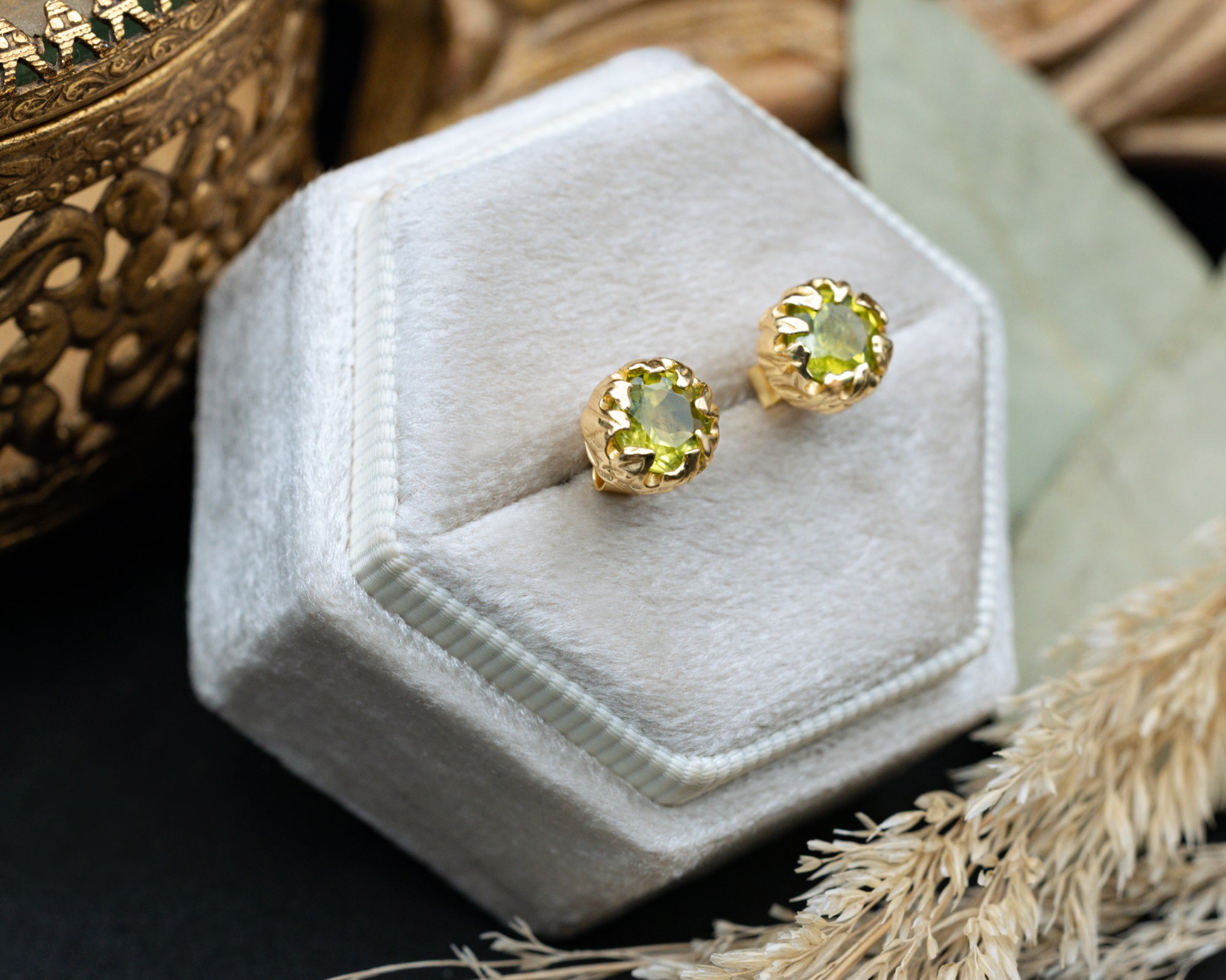 Gold earrings with green peridot on a white hexagonal velvet stand.