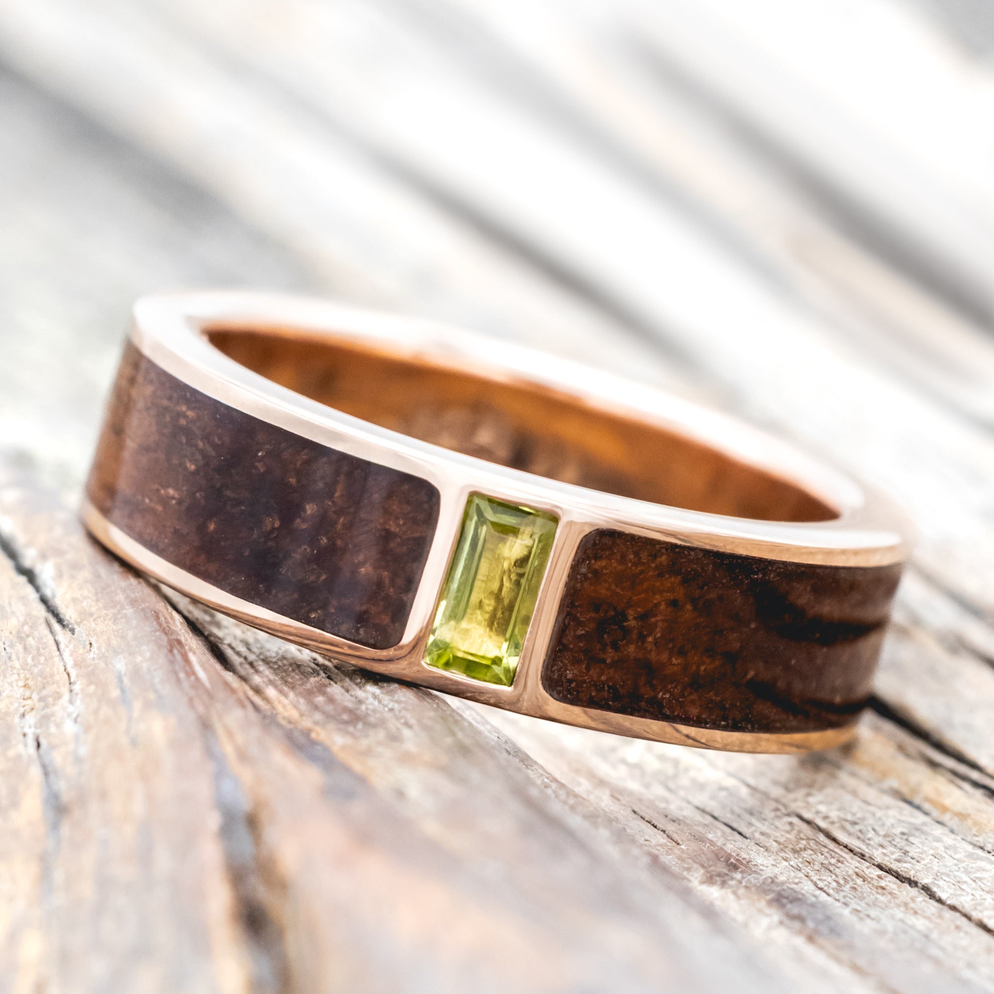 Koa wood ring with a green peridot on a wooden surface