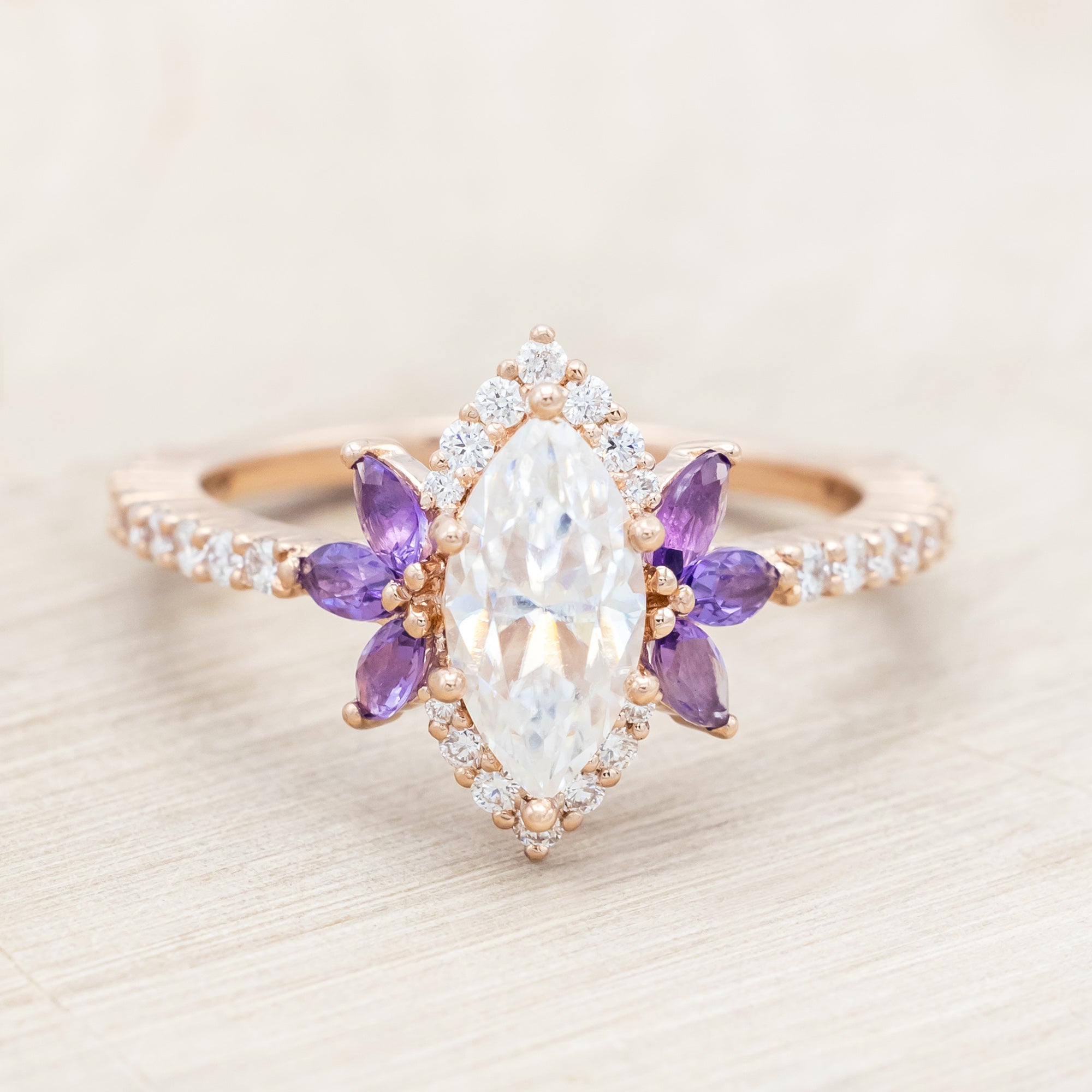 14K Rose gold ring with a moissanite center stone and small purple amethyst accents on a light wooden background