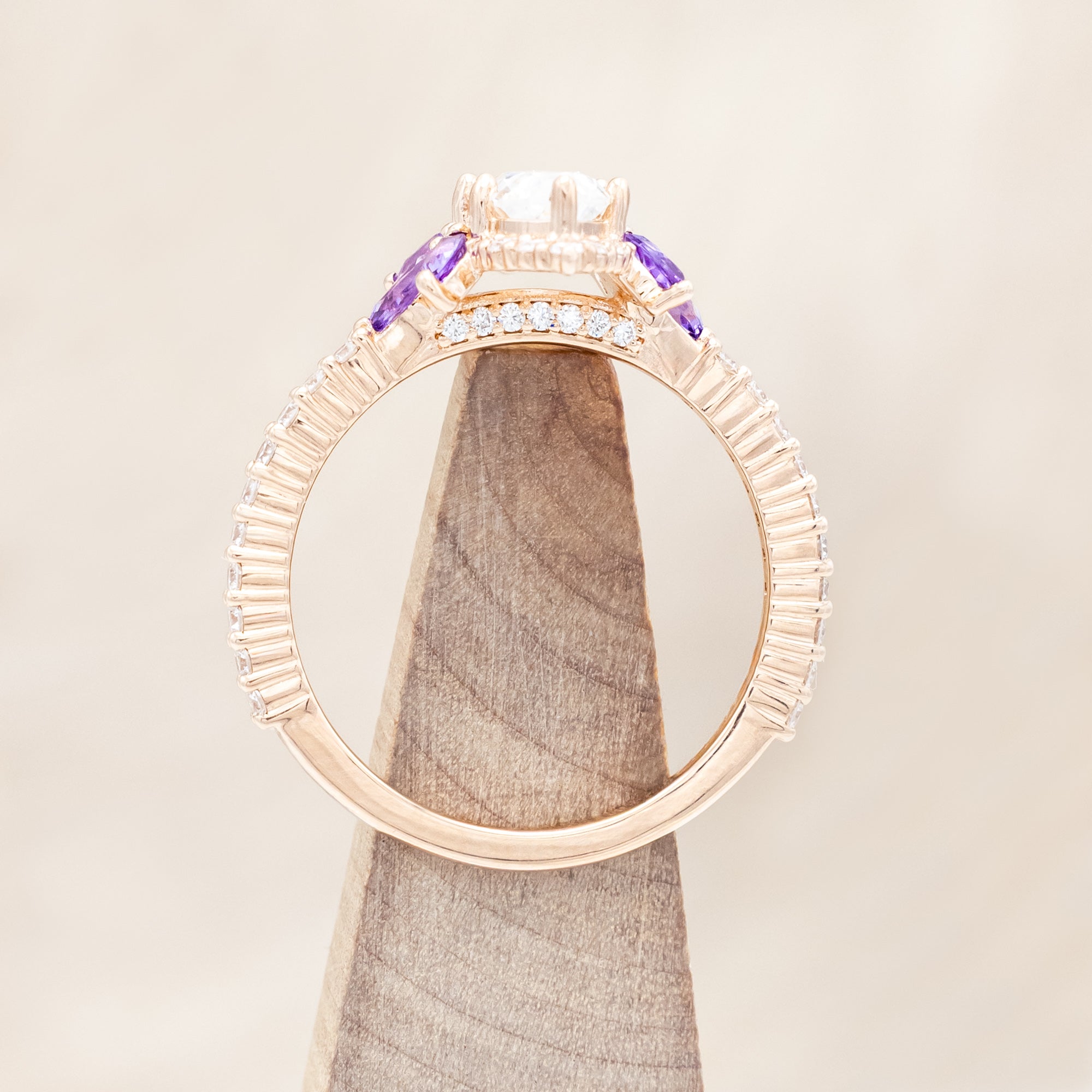 14K Rose gold ring with a moissanite center stone and small purple amethyst accents on a beige background