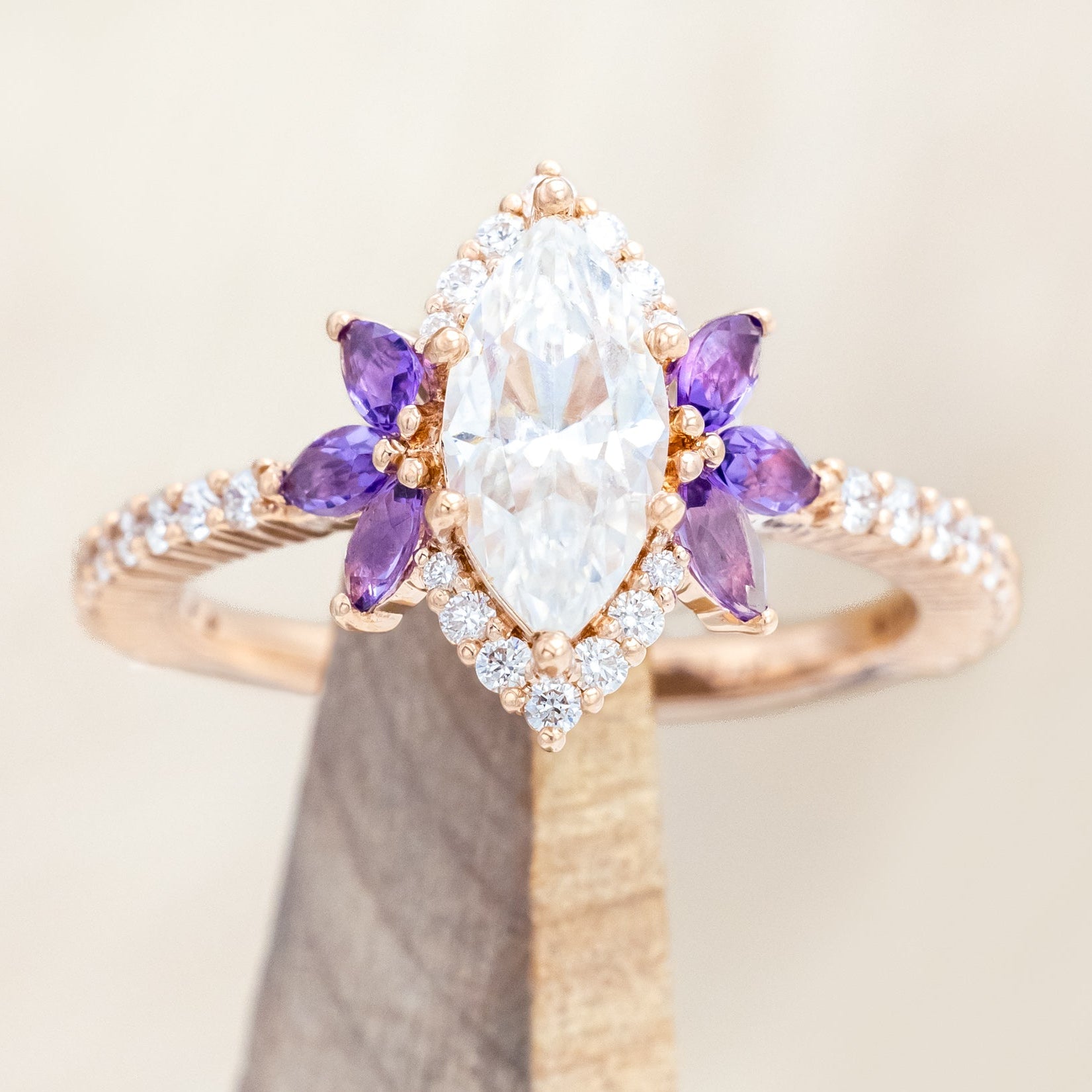 14K Rose gold ring with a moissanite center stone and small purple amethyst accents on a beige background