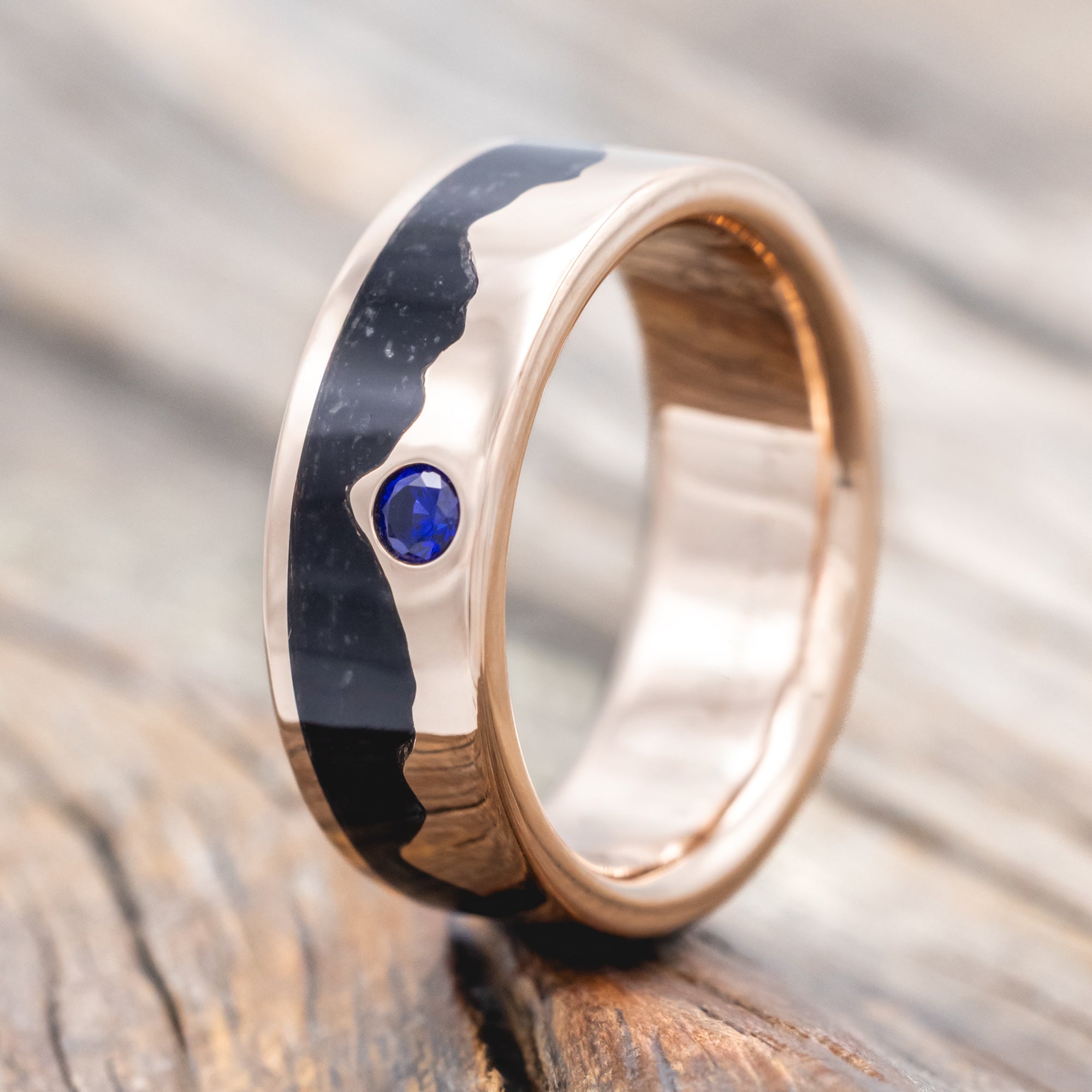 Rose gold ring with black inlay and blue sapphire on a wooden surface