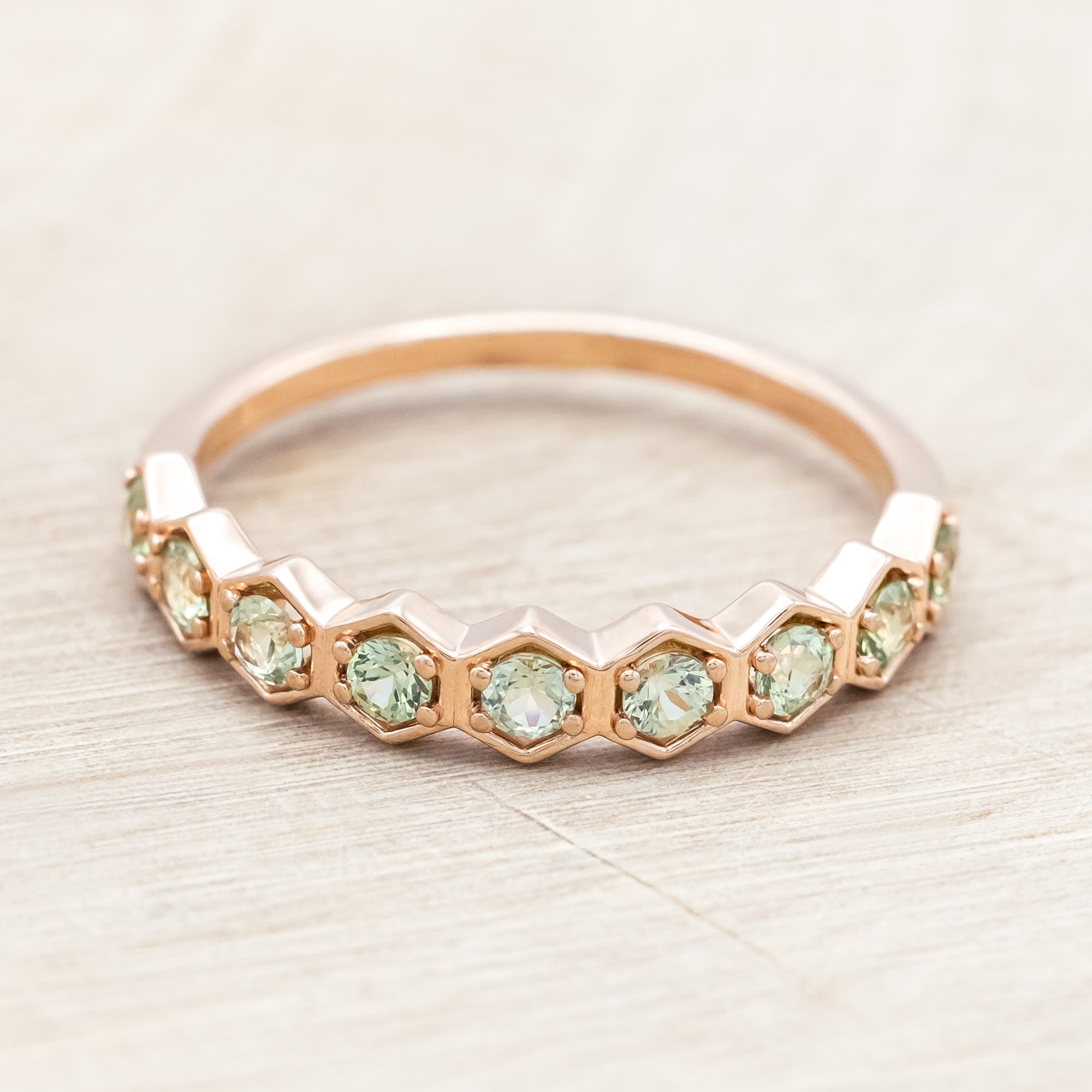 14K rose gold ring with green sapphires on a light wooden surface
