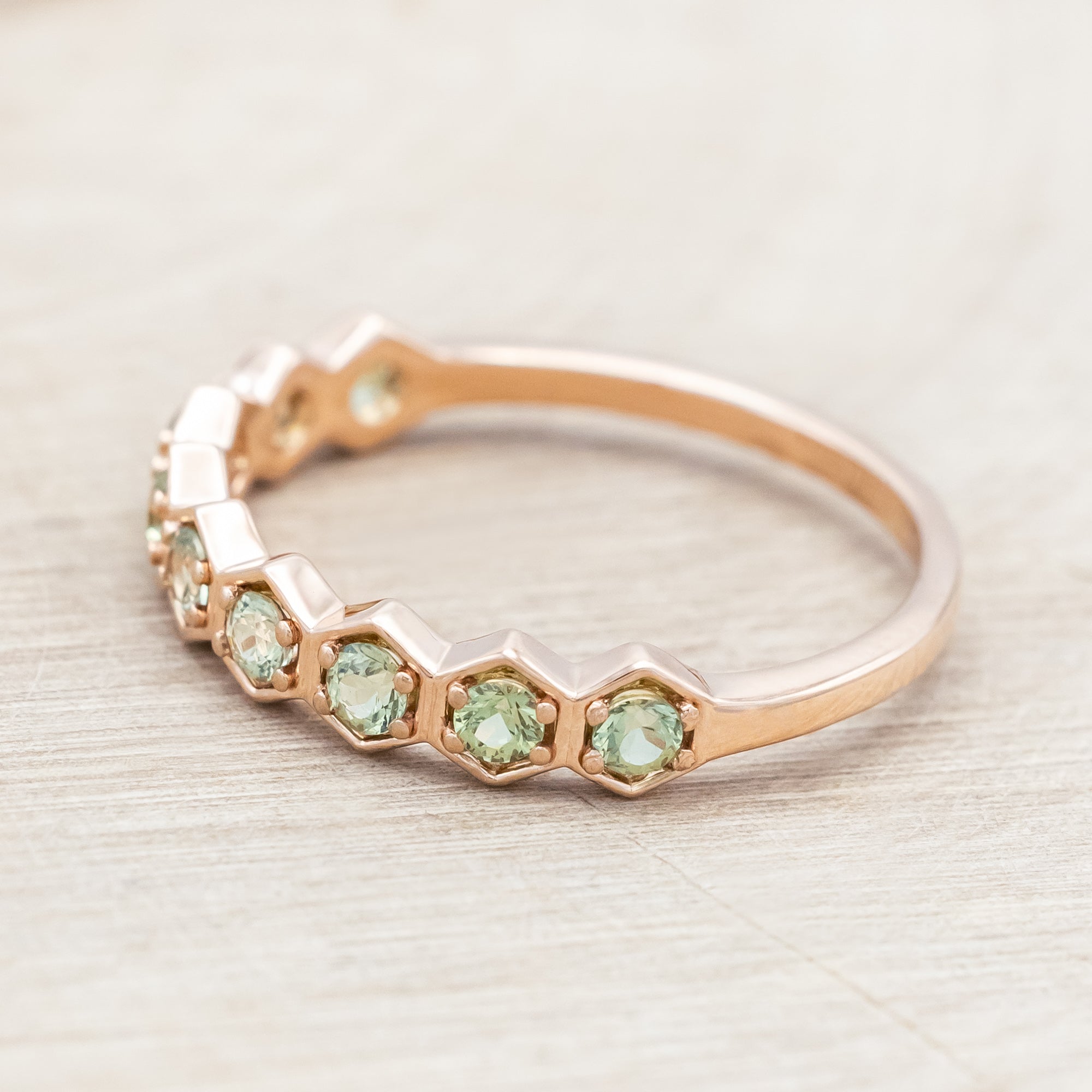 14K rose gold ring with green sapphires on a light wooden surface