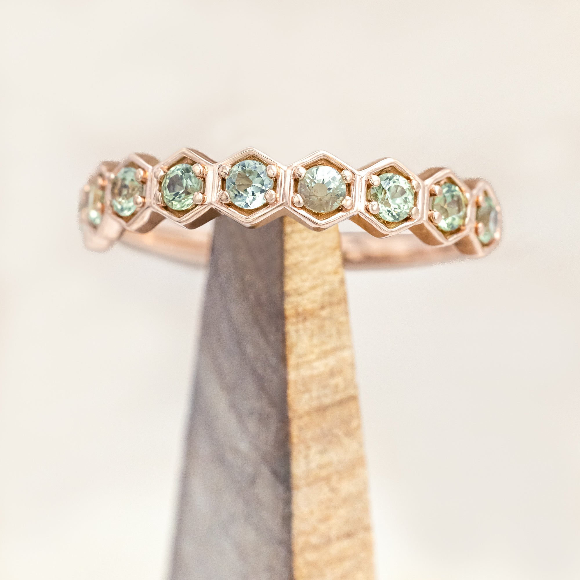 14K rose gold ring with green sapphires on a light background