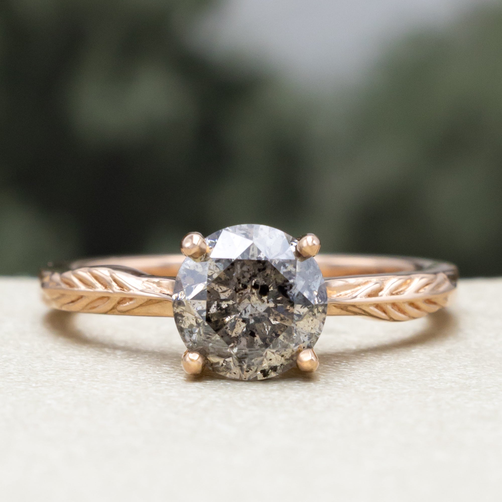 Rose gold ring with round salt & pepper diamond in front of a blurred green background