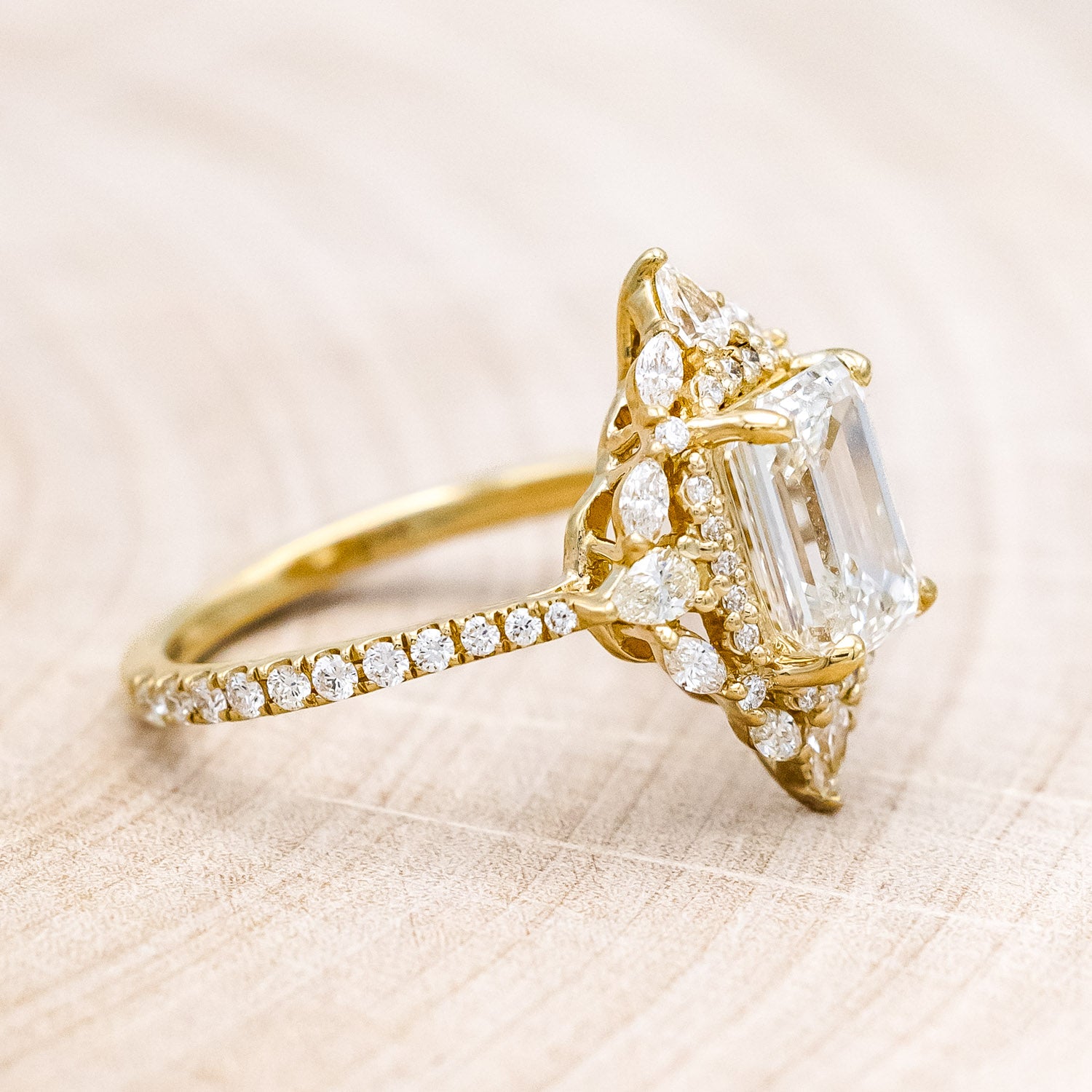 Side view of "North Star" - emerald cut diamond women's engagement ring with a diamond halo and accents on a 14K yellow gold band