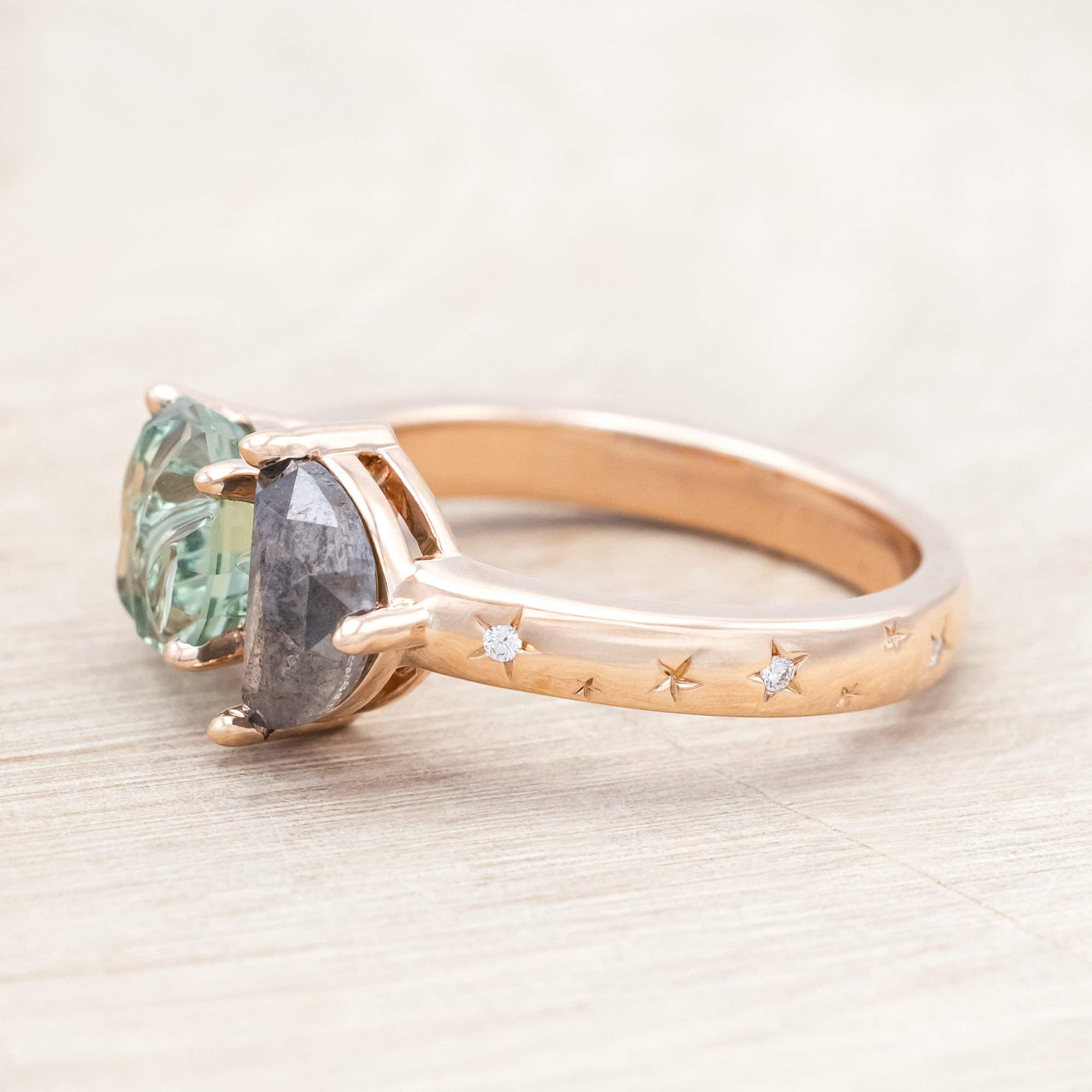 Ring with green sapphire and salt & pepper diamond and rose gold band on a neutral background