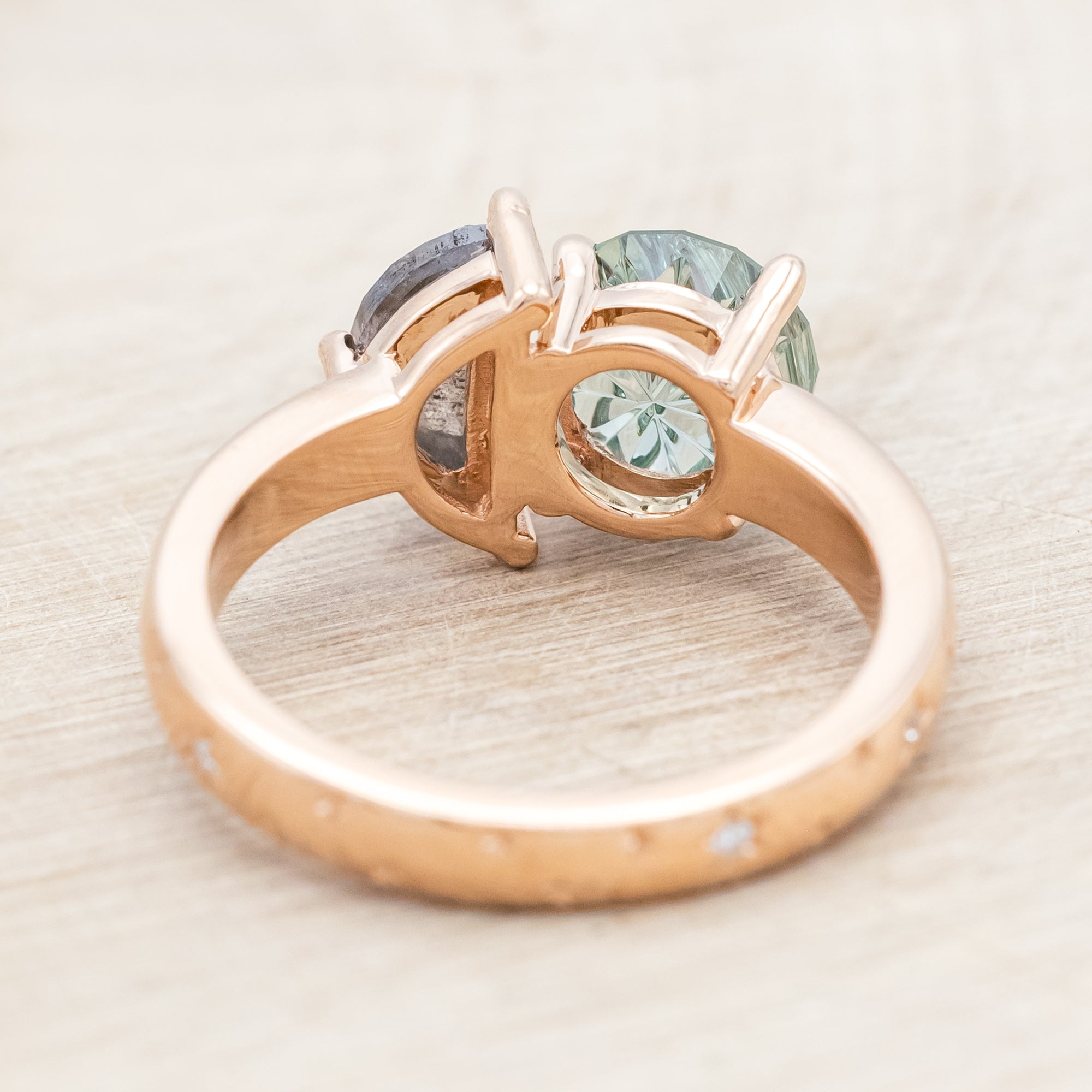 Ring with green sapphire and salt & pepper diamond and rose gold band on a neutral background