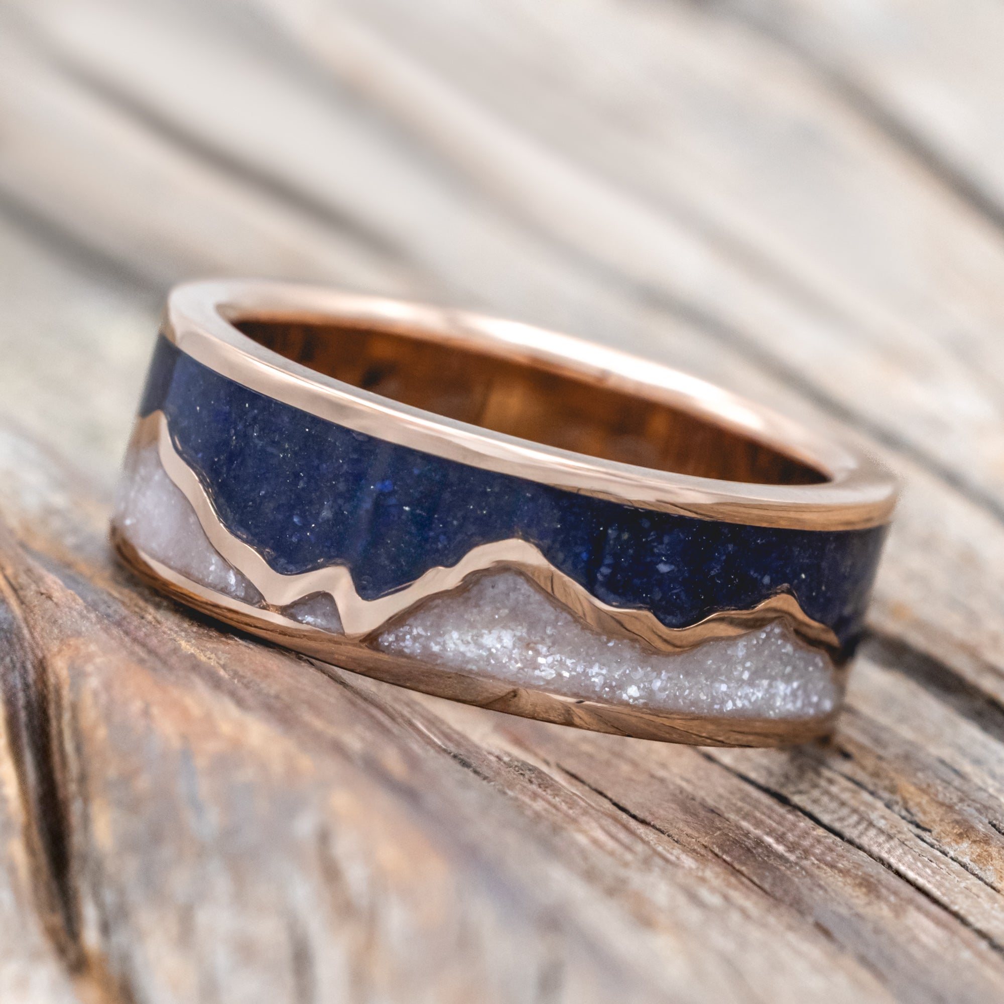 Rose gold ring with lapis lazuli and diamond dust inlay on a wooden surface