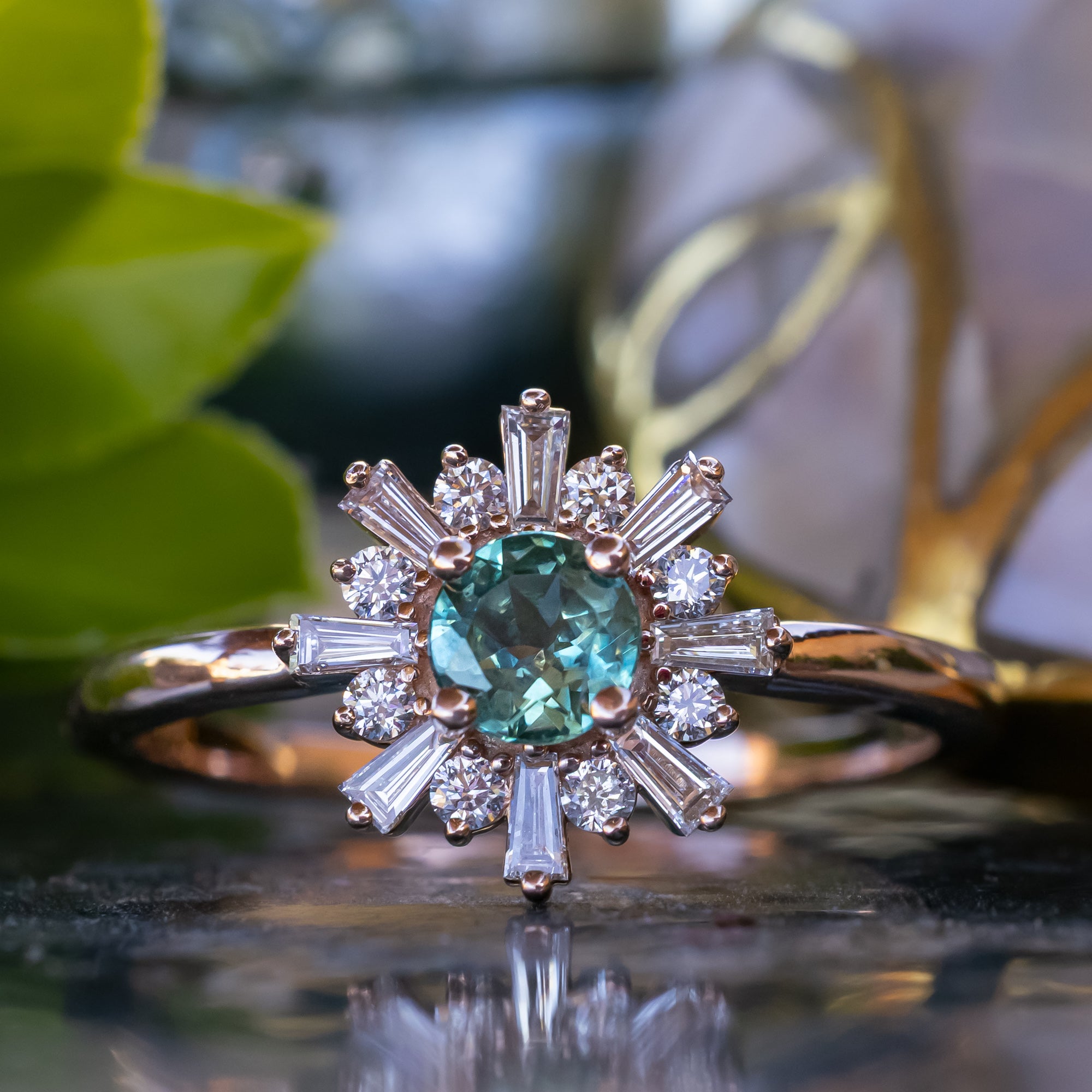 Rose gold ring with a Montana sapphire and diamond accents on a reflective surface.