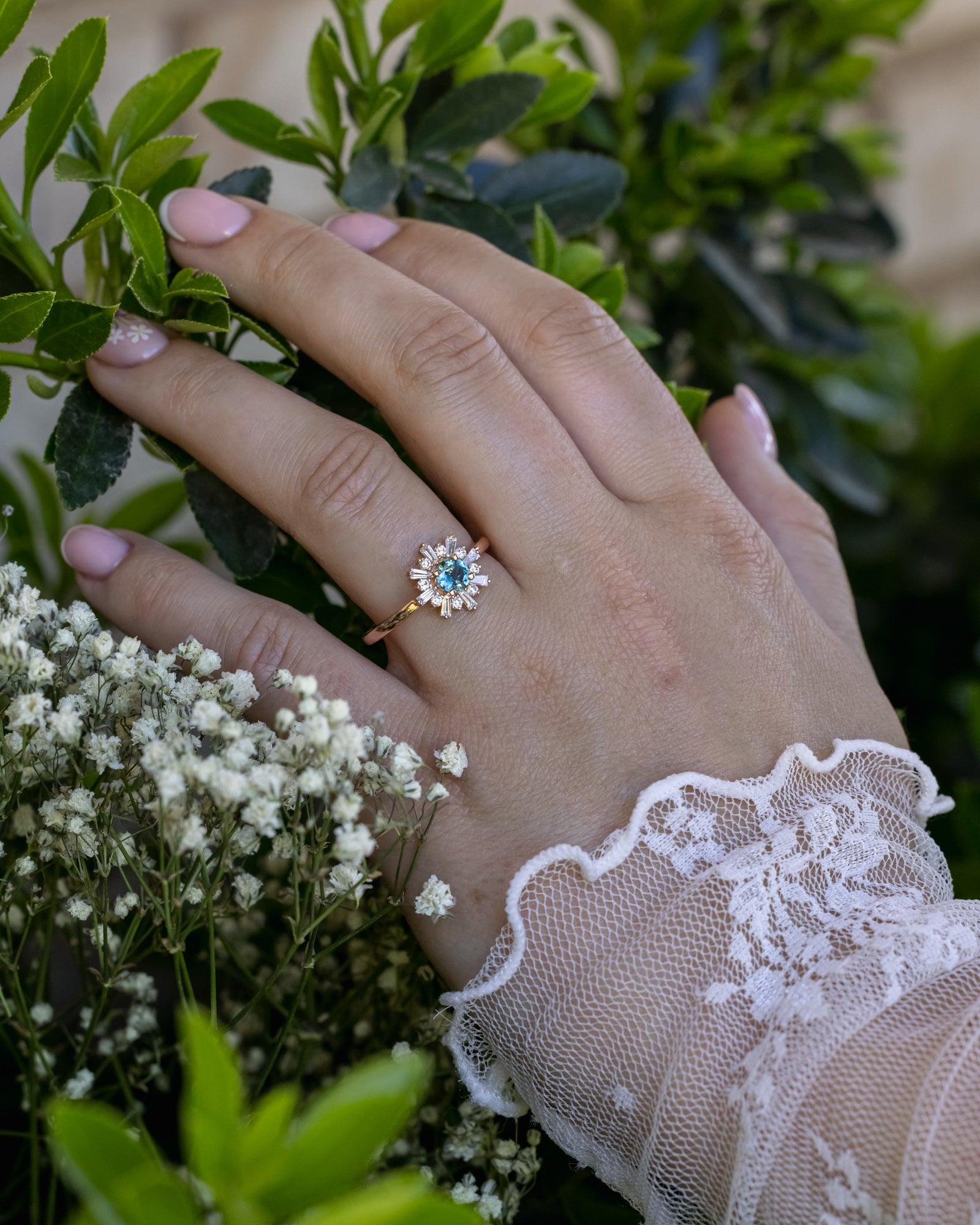 Hand wearing a ring with a Montana sapphire, surrounded by greenery and flowers.
