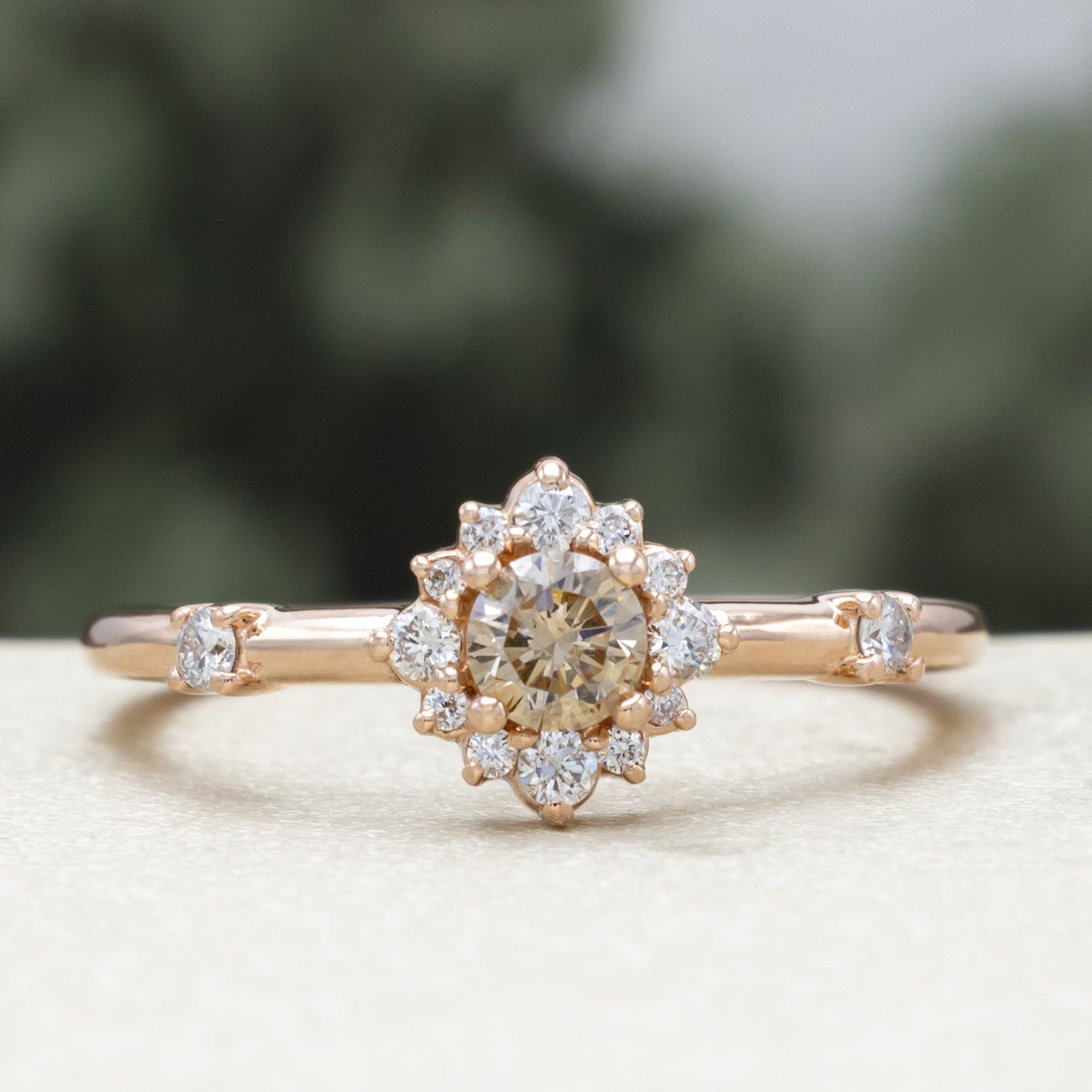 Salt and pepper rose gold ring with diamond halo on a blurred green background