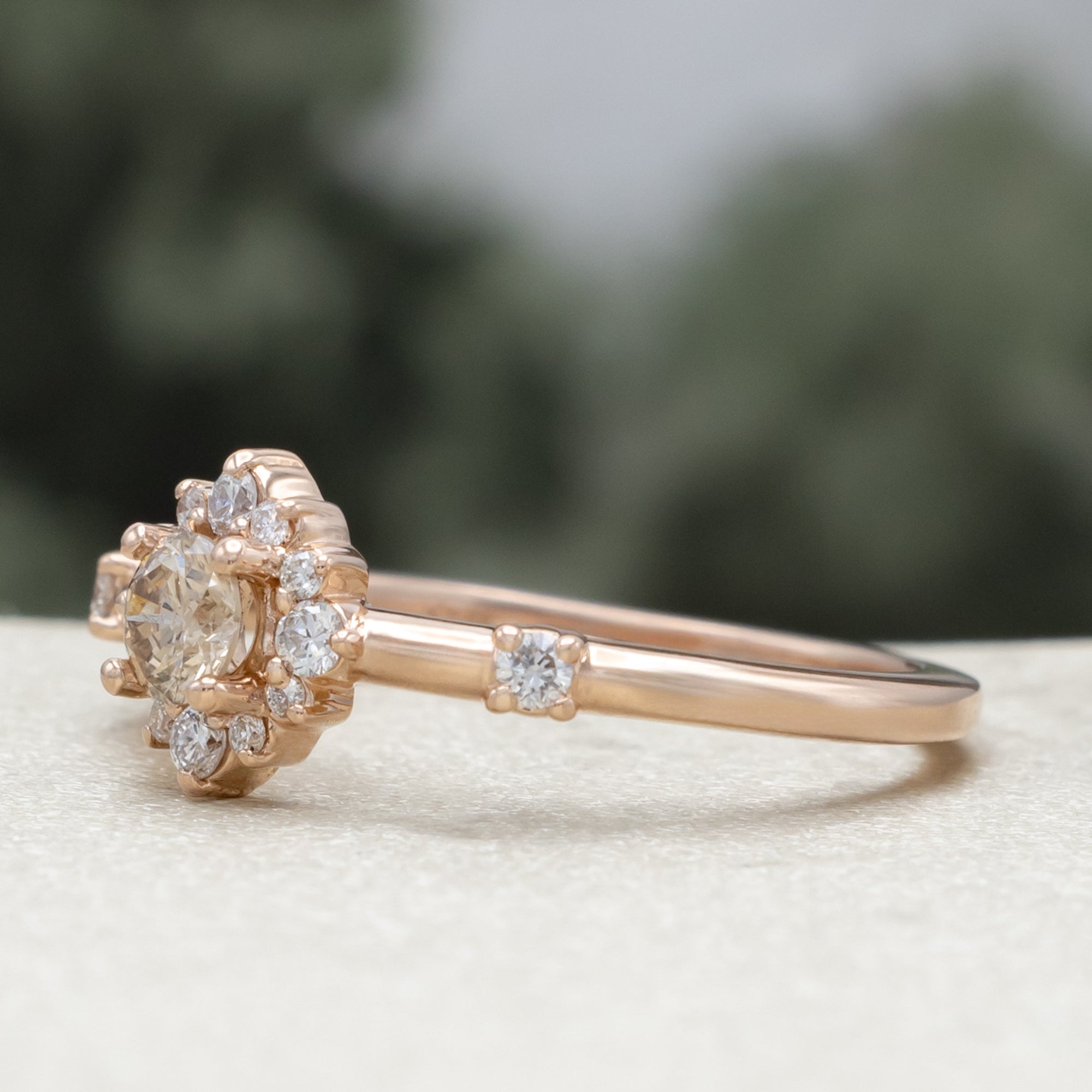Salt and pepper rose gold ring with diamond halo on a blurred green background