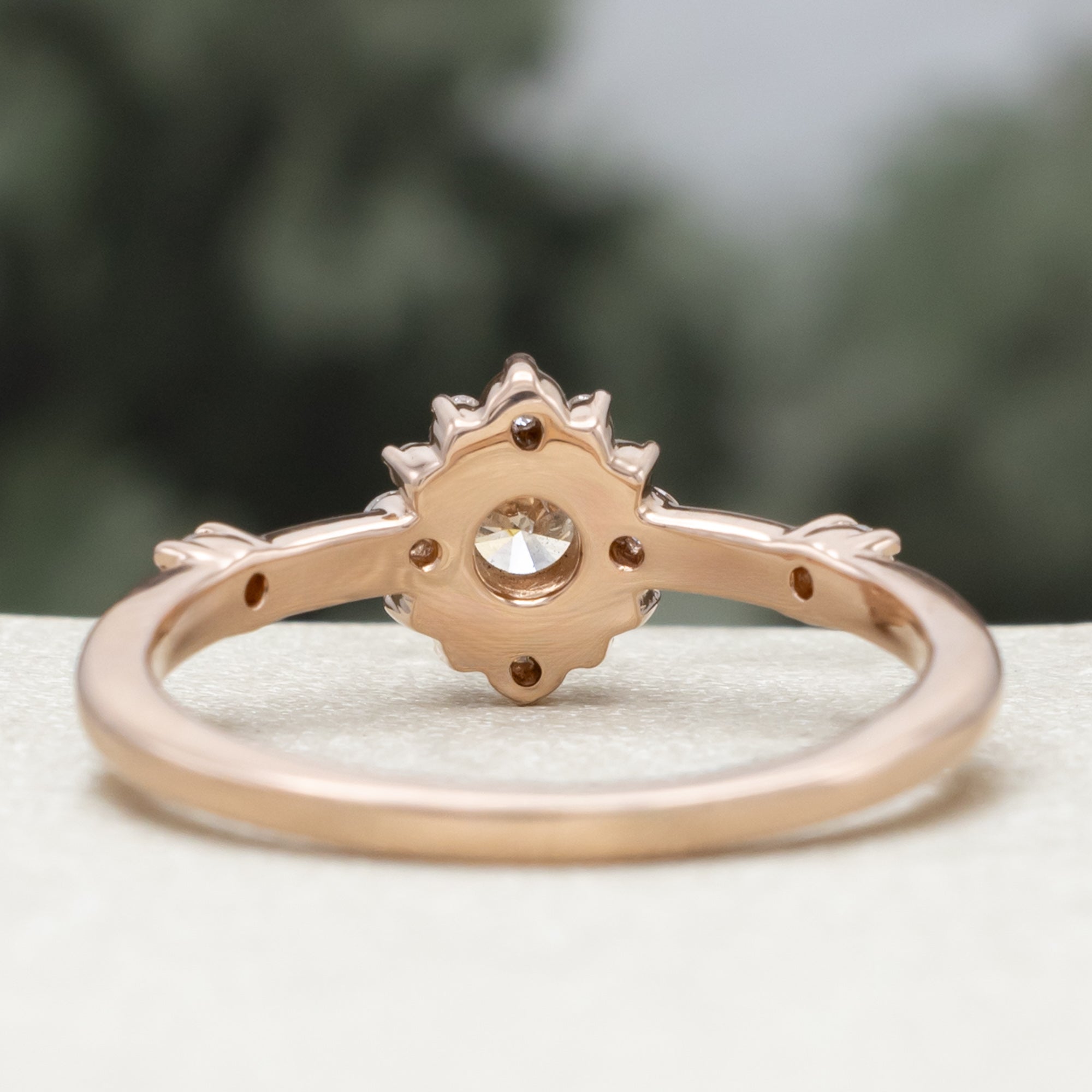 Salt and pepper rose gold ring with diamond halo on a blurred green background