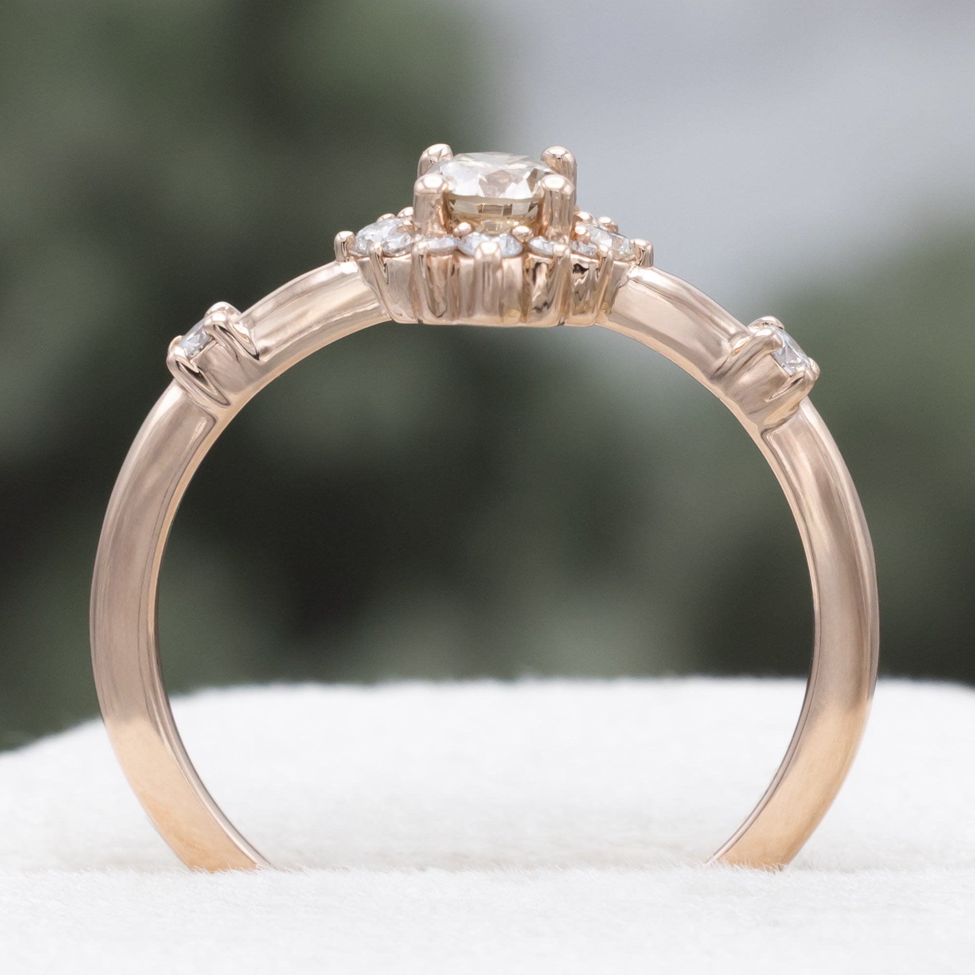 Salt and pepper rose gold ring with diamond halo on a blurred green background