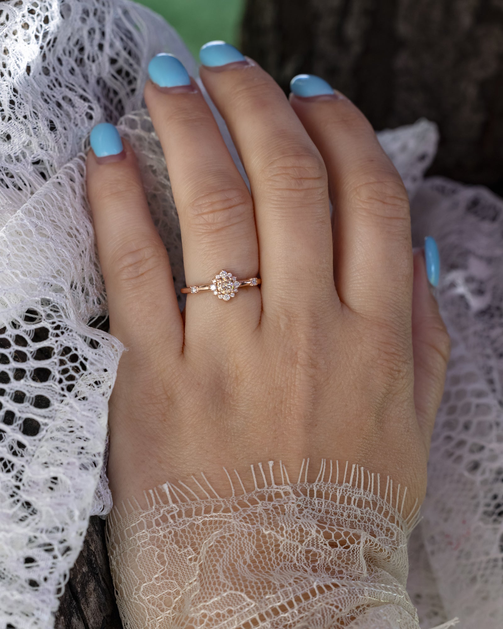 Hand wearing a rose gold ring with a champagne diamond and a diamond halo with a lace sleeve