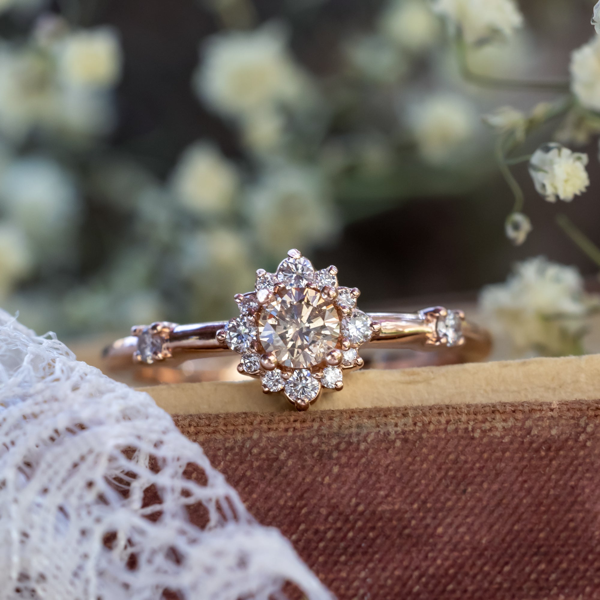 Rose gold ring with a champagne diamond and diamond halo on a decorative surface.