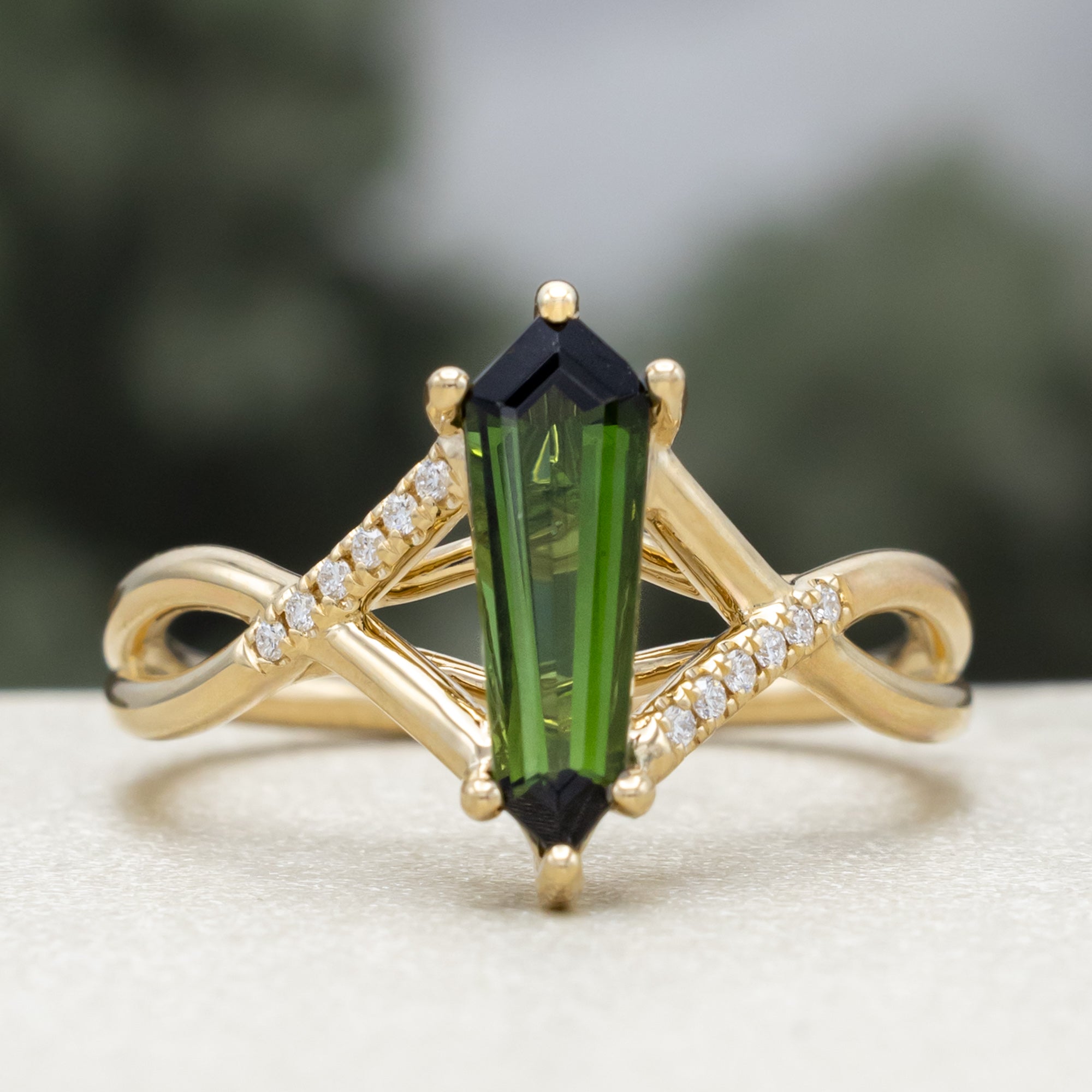 Gold ring with a green tourmaline and diamond accents against a blurred green background