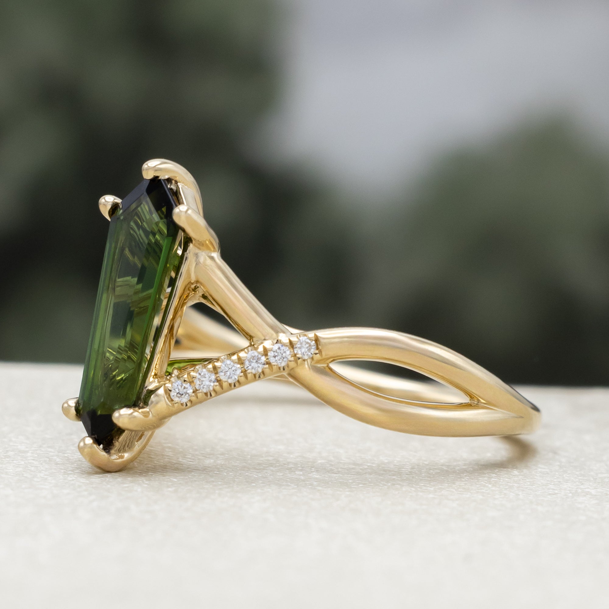 Gold ring with a green tourmaline and diamond accents against a blurred green background