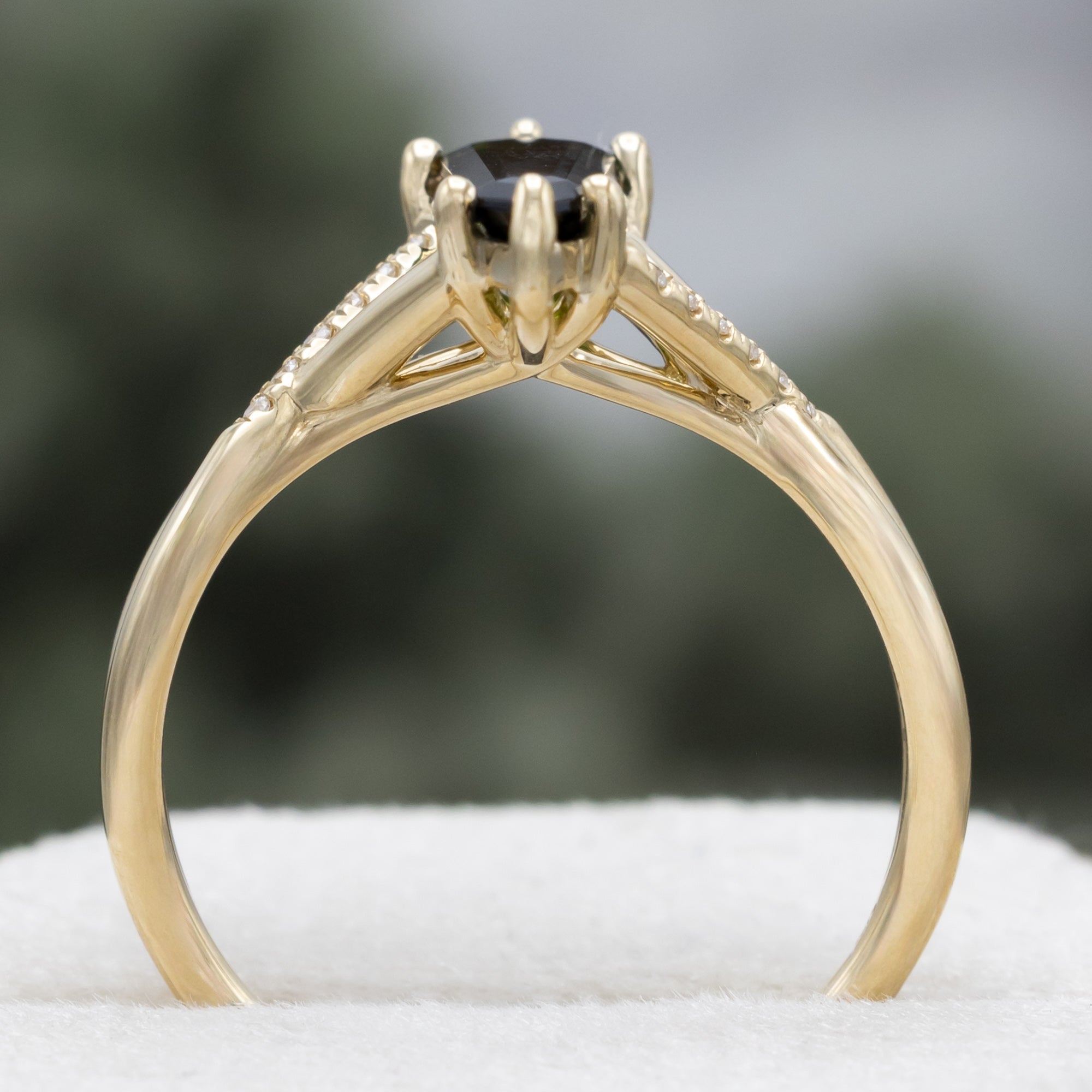 Gold ring with a green tourmaline and diamond accents against a blurred green background